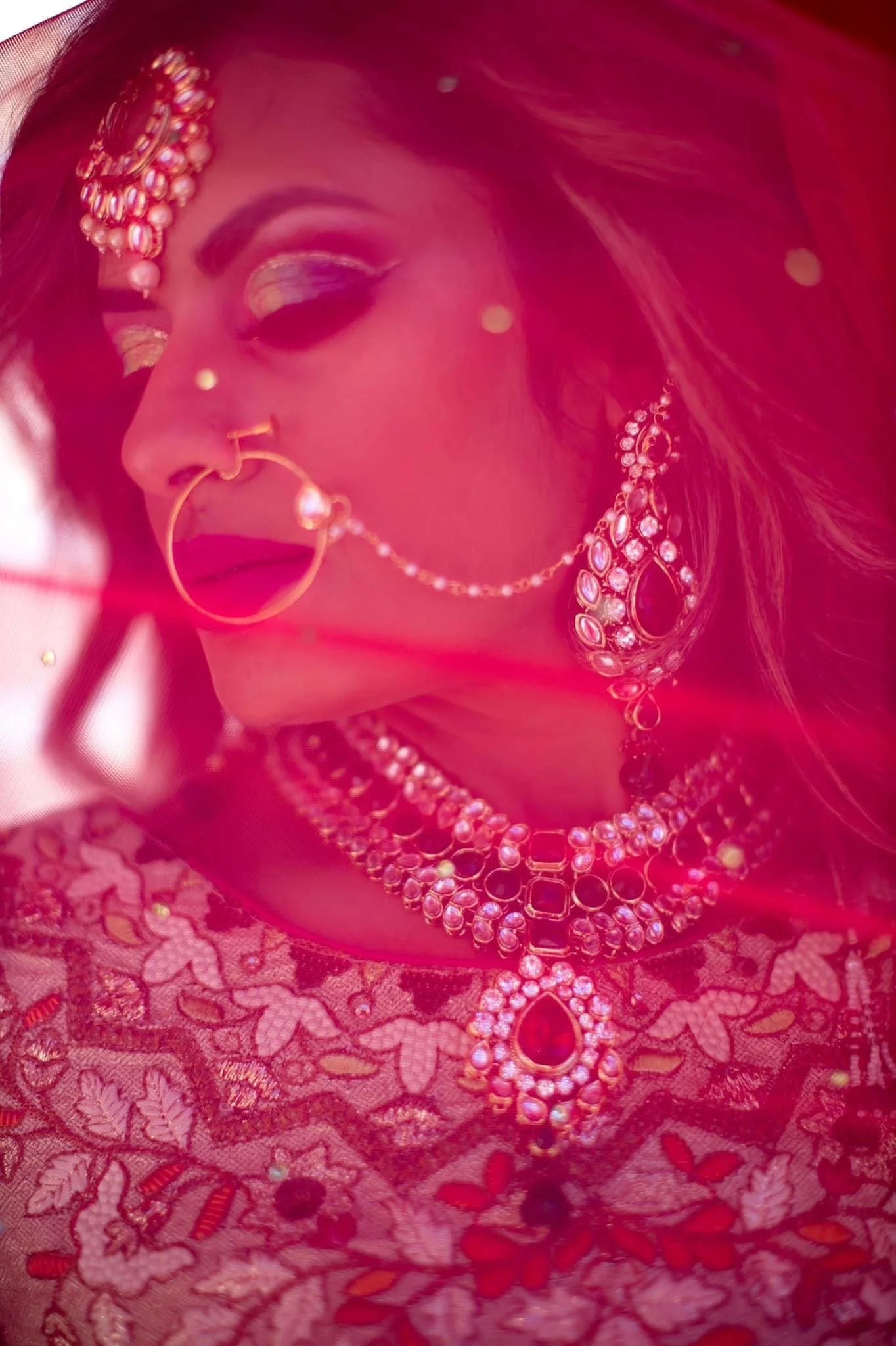 woman with face jewelry behind red vail 