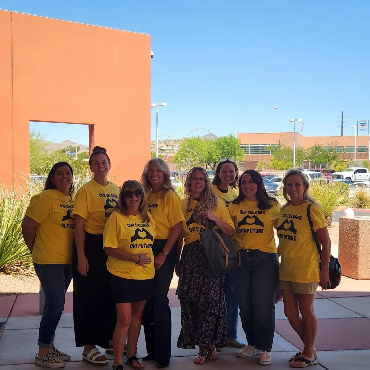 Group of women standing outdoors, wearing yellow T-shirts with the message 'Our Children, Our Future', smiling for the camera.