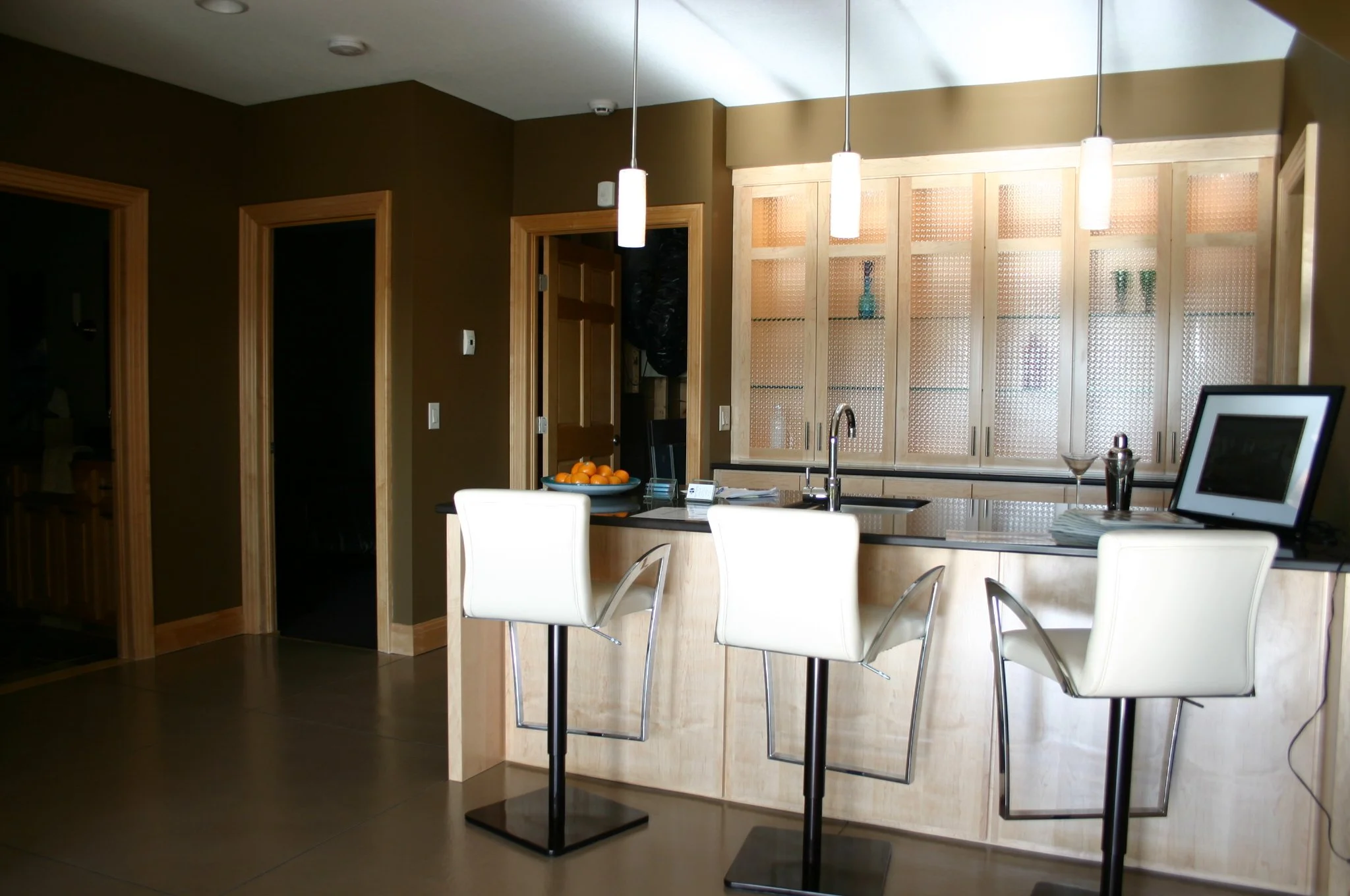 A modern cocktail bar with a lakeside view, well-lit by pendants from above and shelves from behind.