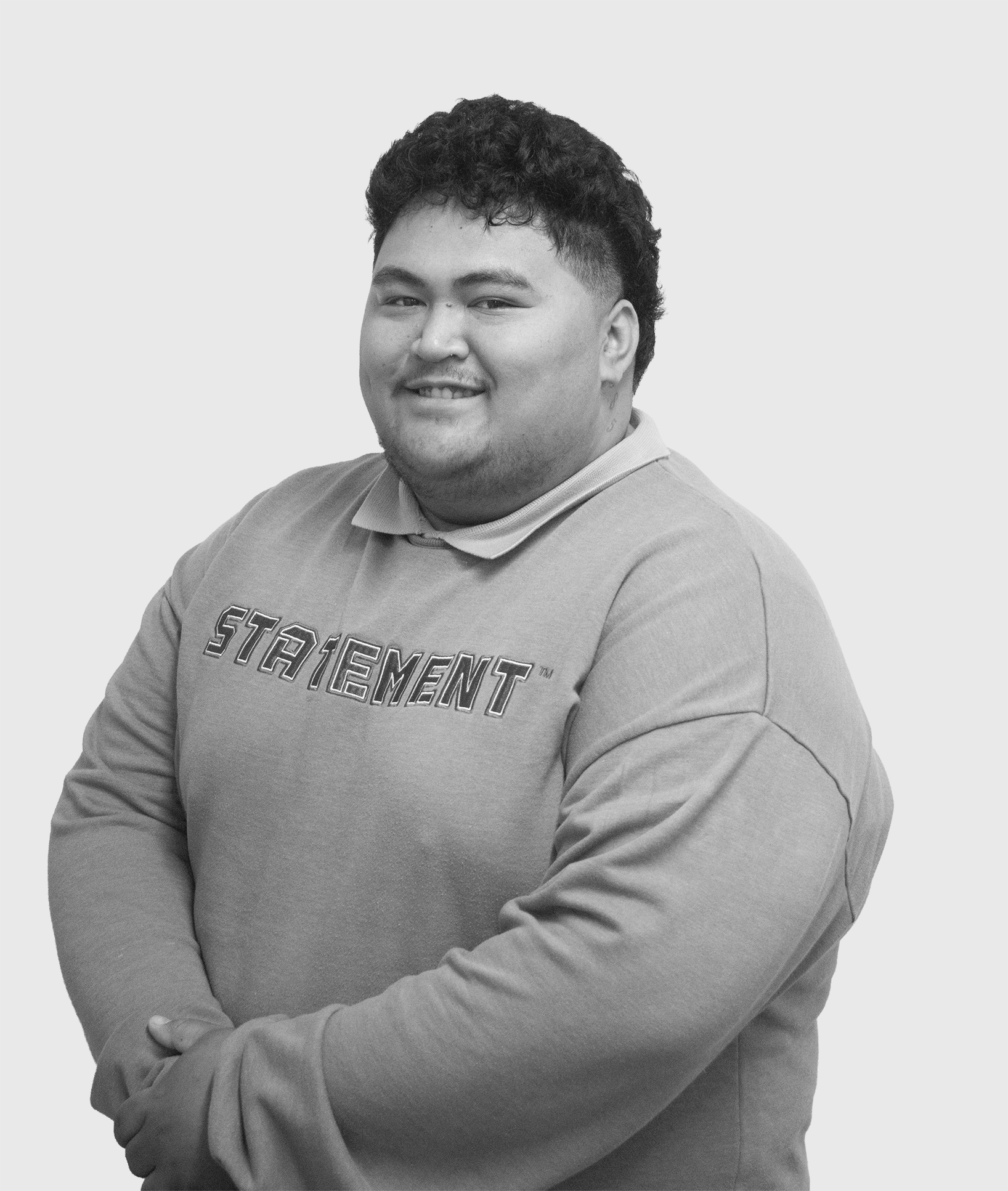 Black and white portrait of a smiling young man with curly hair, wearing a sweatshirt that says "STATEMENT".