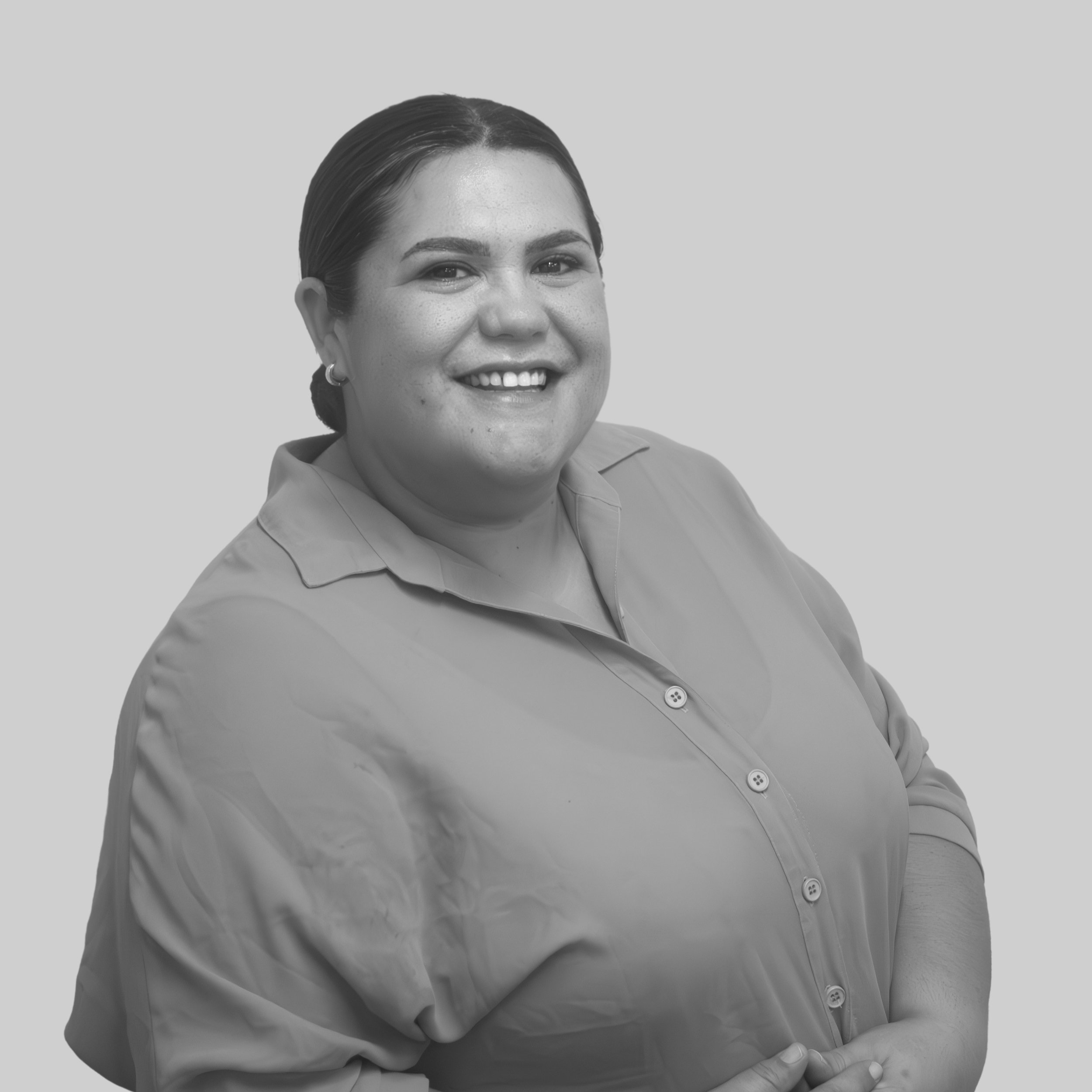 Black and white photo of a smiling woman with dark hair in a bun, wearing earrings and a collared shirt, with arms crossed