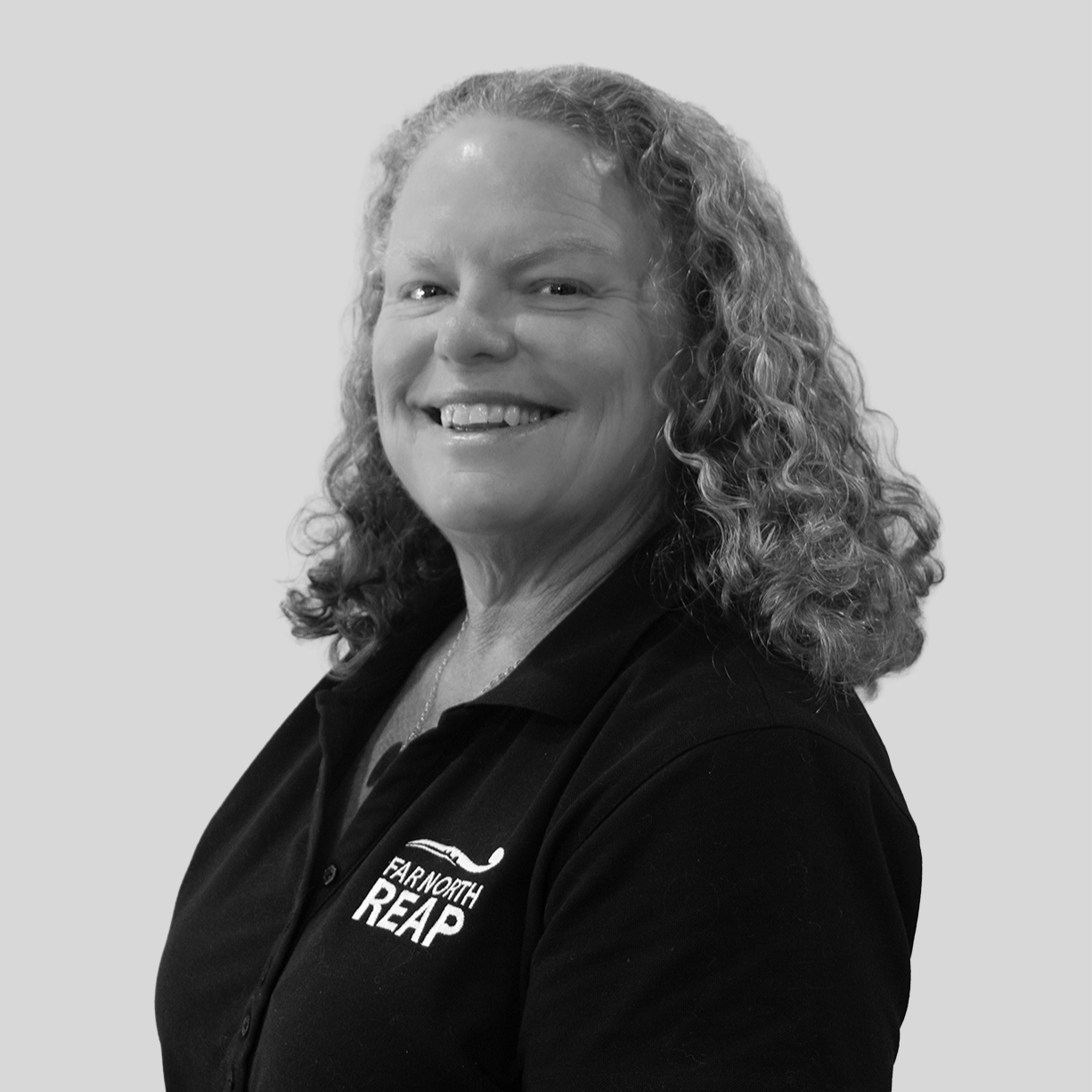 Black and white photo of a woman with long curly hair smiling, wearing a patterned blouse against a plain background.