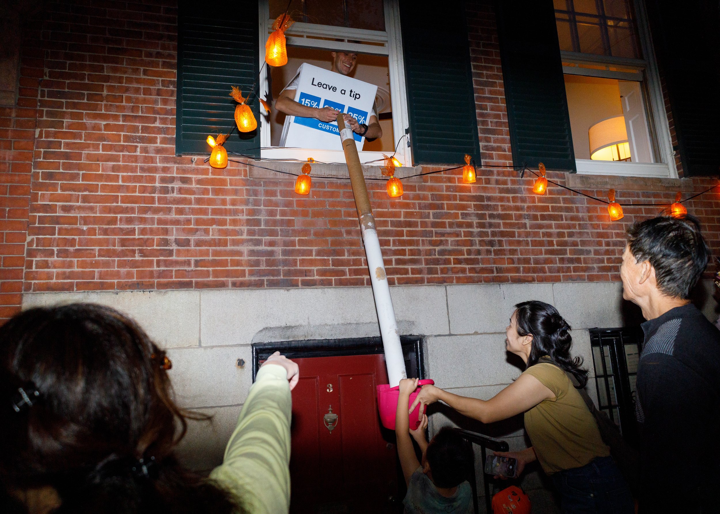 Boston, MA: October 31st, 2024: A Beacon Hill resident slides pieces of candy down a chute to a child's candy bucket.