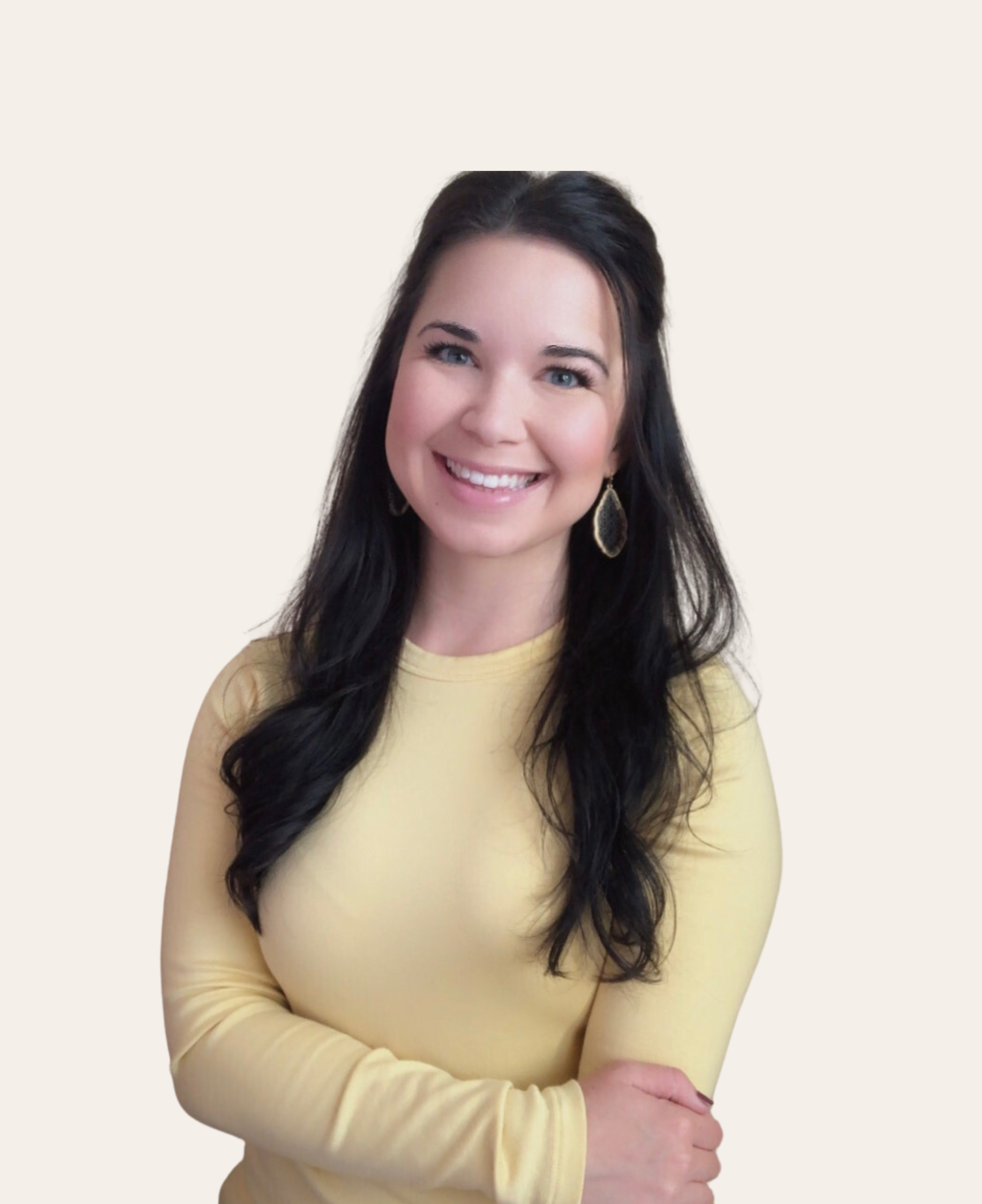 A smiling woman with long dark hair wearing a yellow long-sleeve shirt and dangling earrings against a plain background.