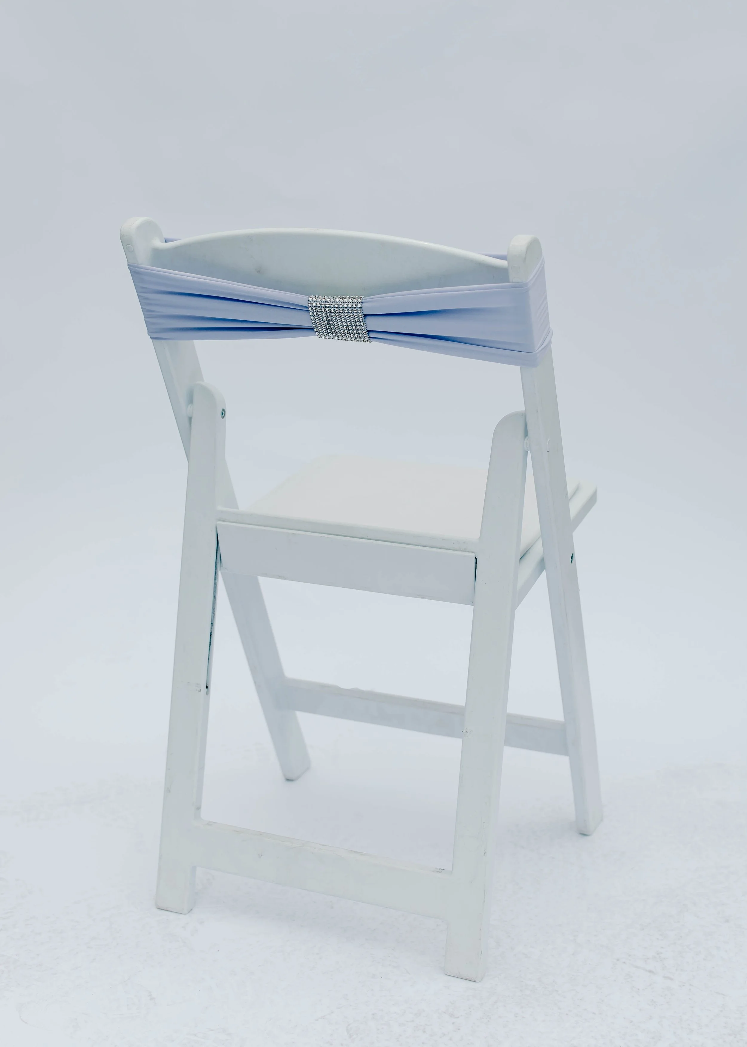 White wooden high chair with a light blue sash tied around its backrest, decorated with a silver rhinestone band, set against a plain light background.