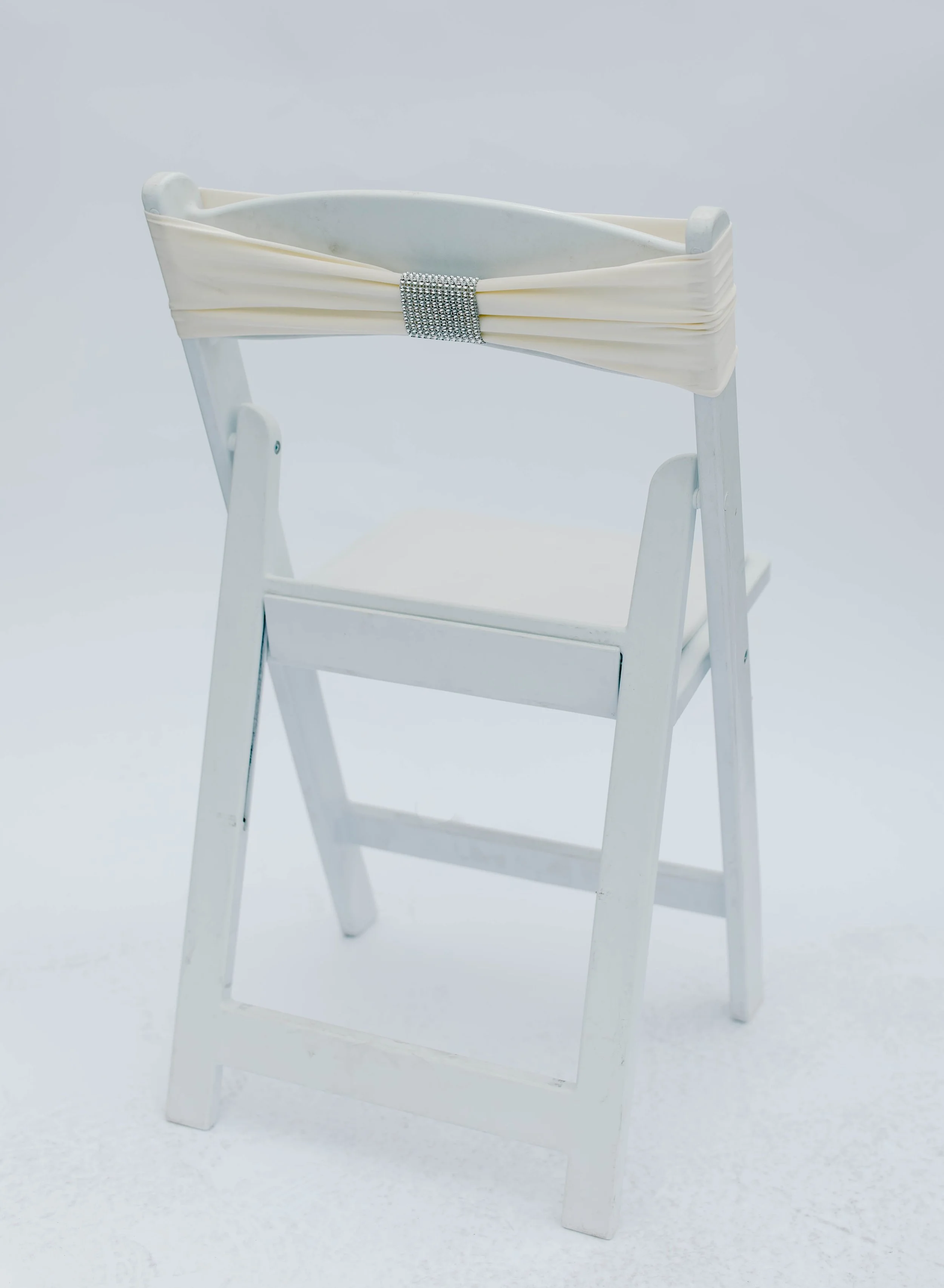 White wooden high chair with a decorative cream-colored fabric drape tied with a silver rhinestone band across the top.