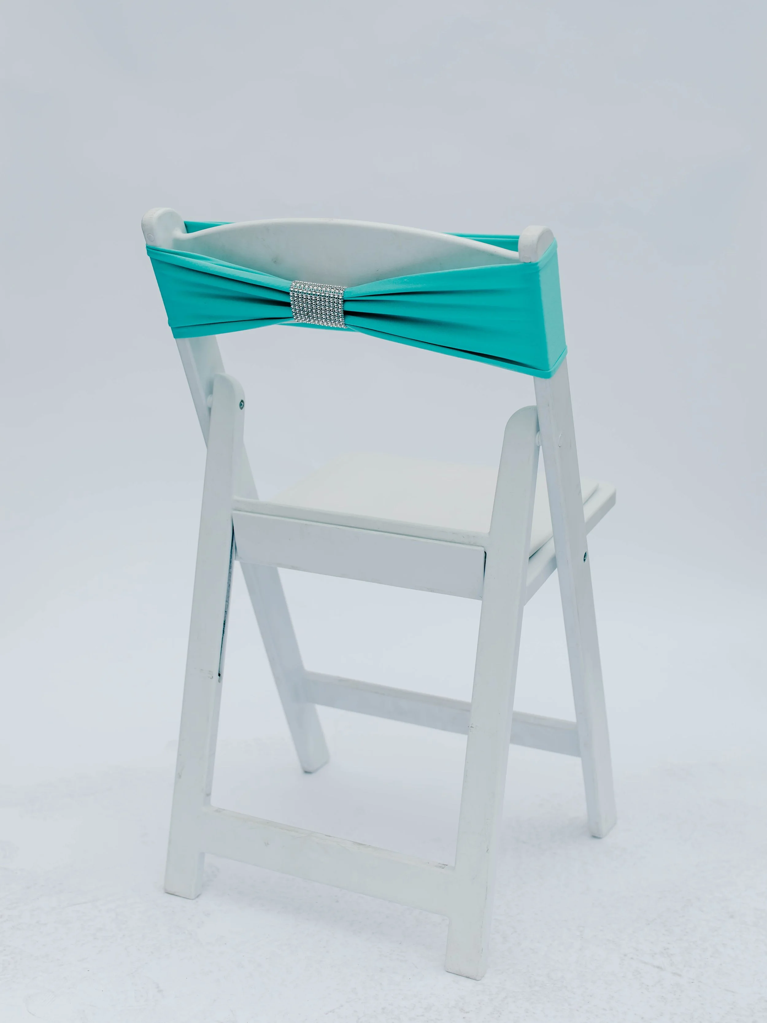 White wooden high chair with a turquoise fabric sash secured with a rhinestone band around the top.