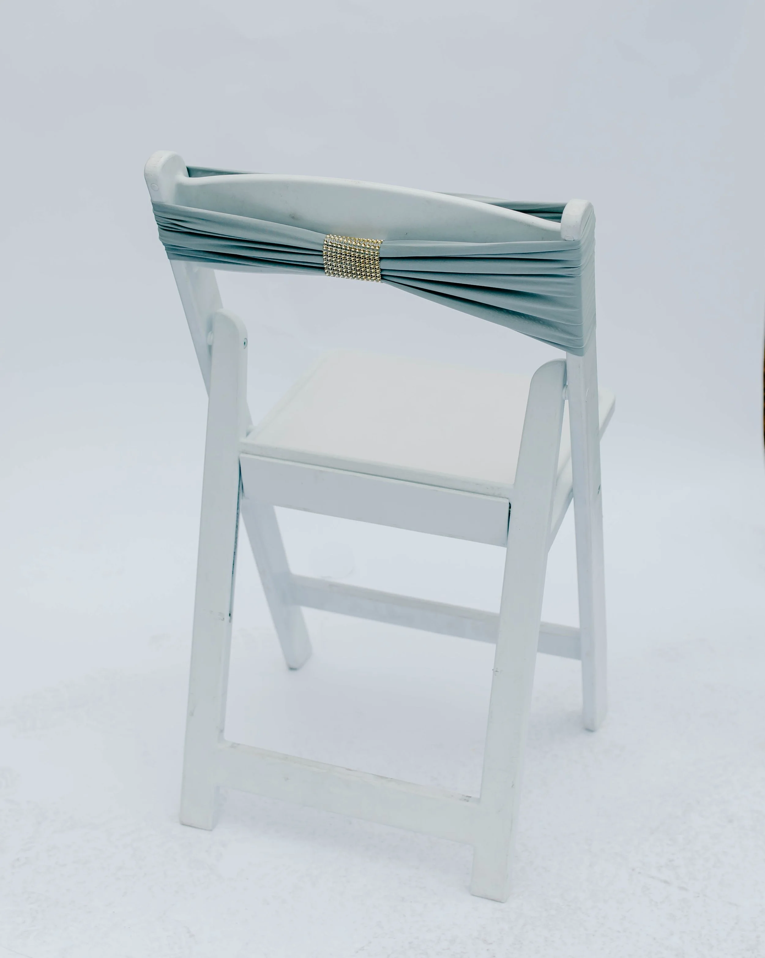 White wooden chair with a light grey pleated sash draped over the backrest and secured with a decorative band.
