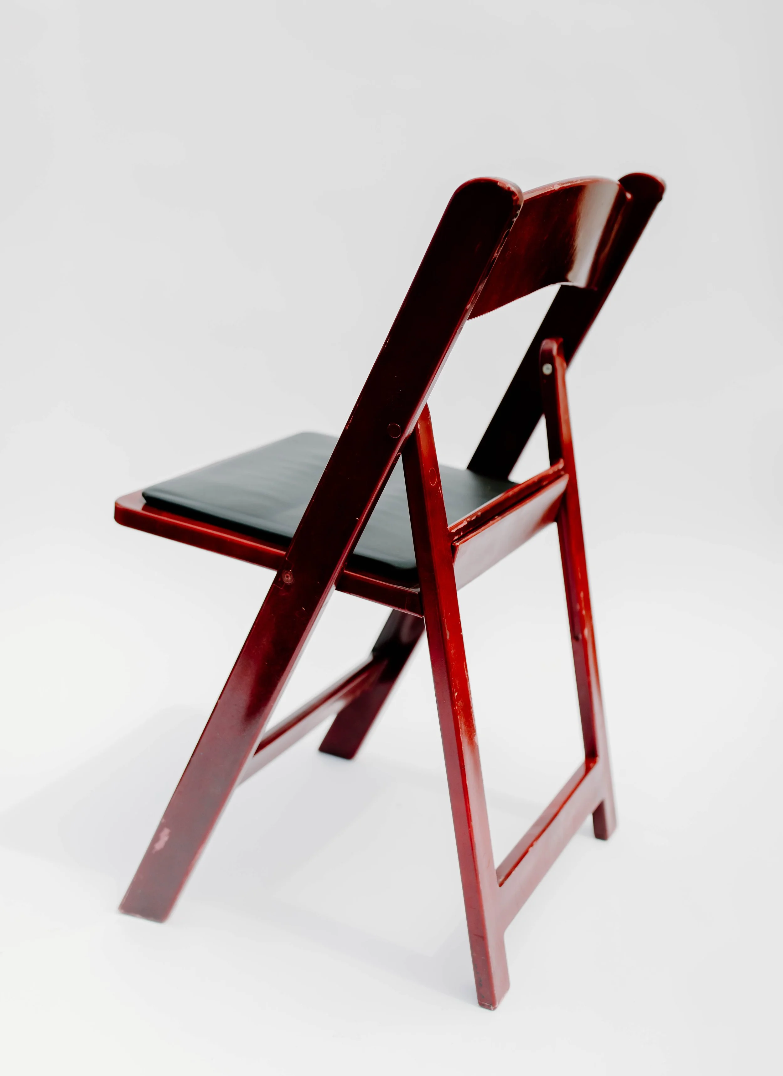 Red wooden folding chair with a black seat on a plain white background.