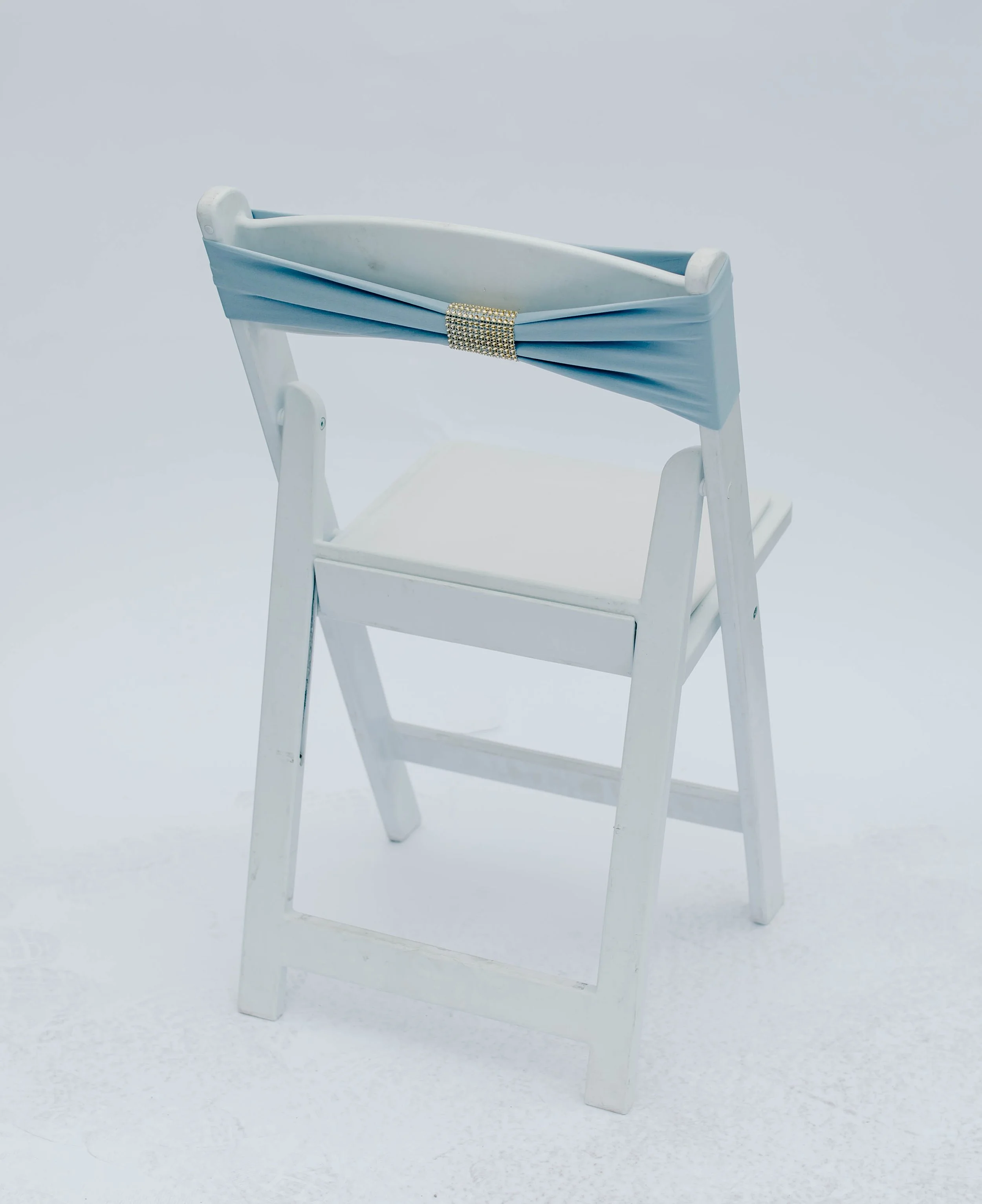 White wooden high chair with a blue fabric sash tied around the backrest, decorated with a rhinestone buckle.