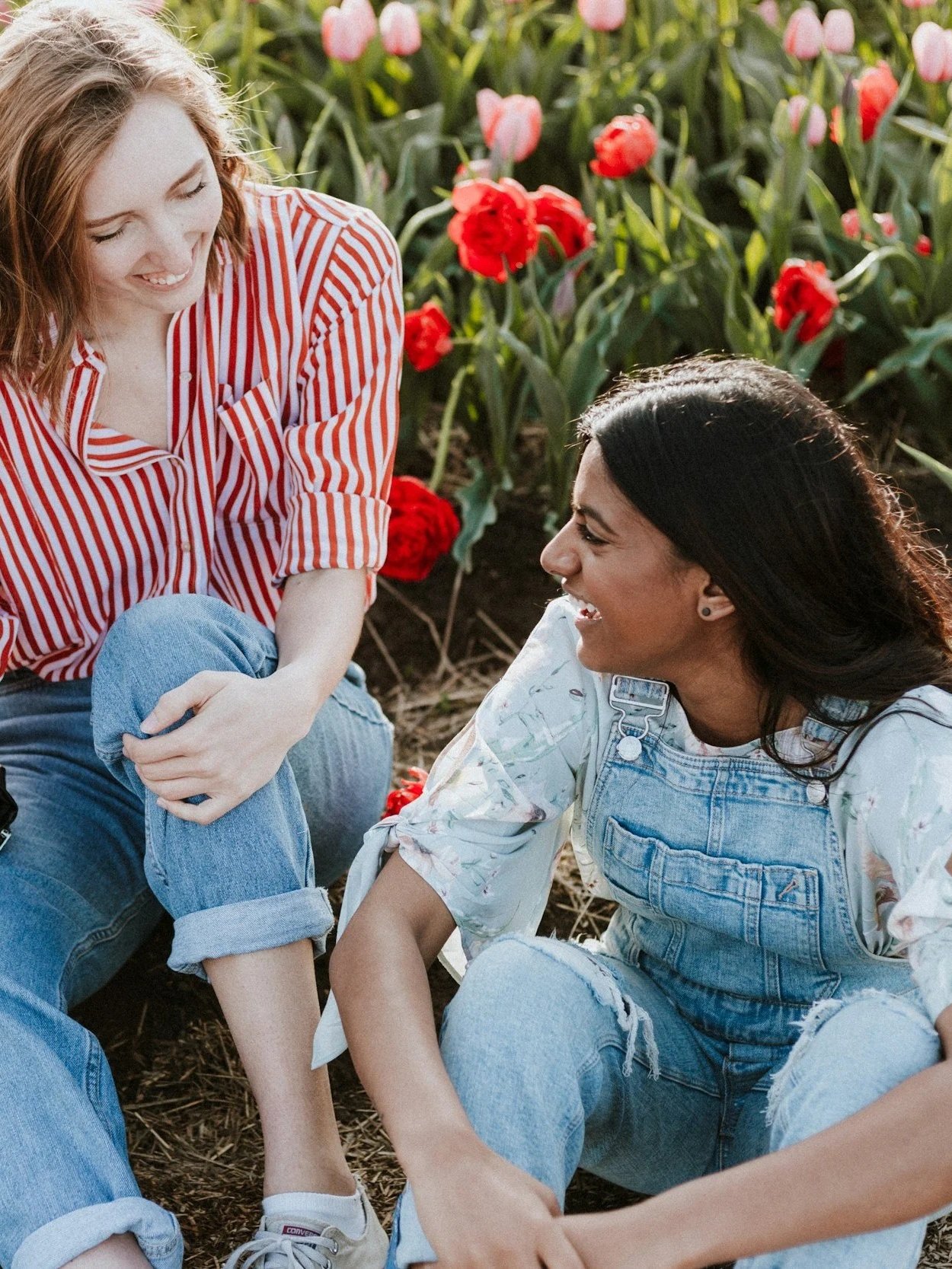 Two women sitting in a tulip flower garden, smiling and enjoying each other's company.