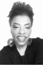 Close-up black and white portrait of a woman with short, curly hair, wearing large earrings and a black top, smiling slightly.