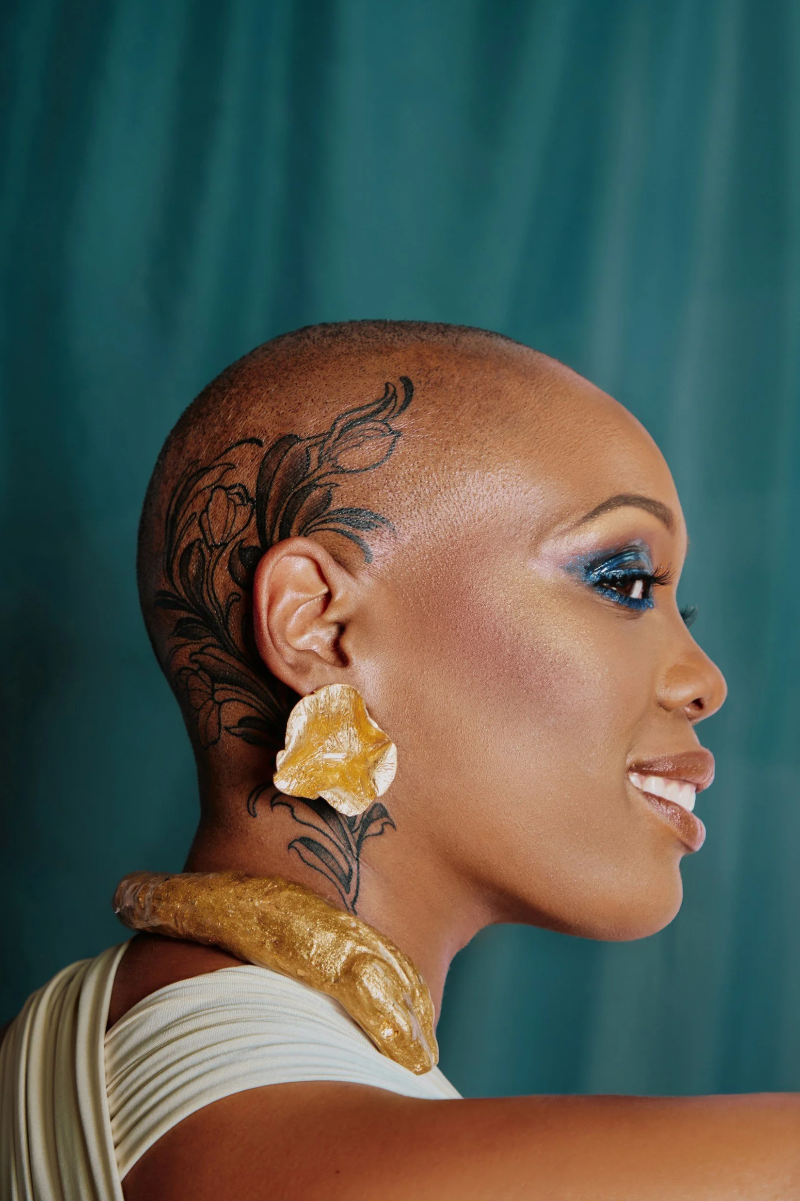 Bald head black women with head tattoo and beautiful makeup wearing La Corneille jewelry by Montreal designer Scarlet James