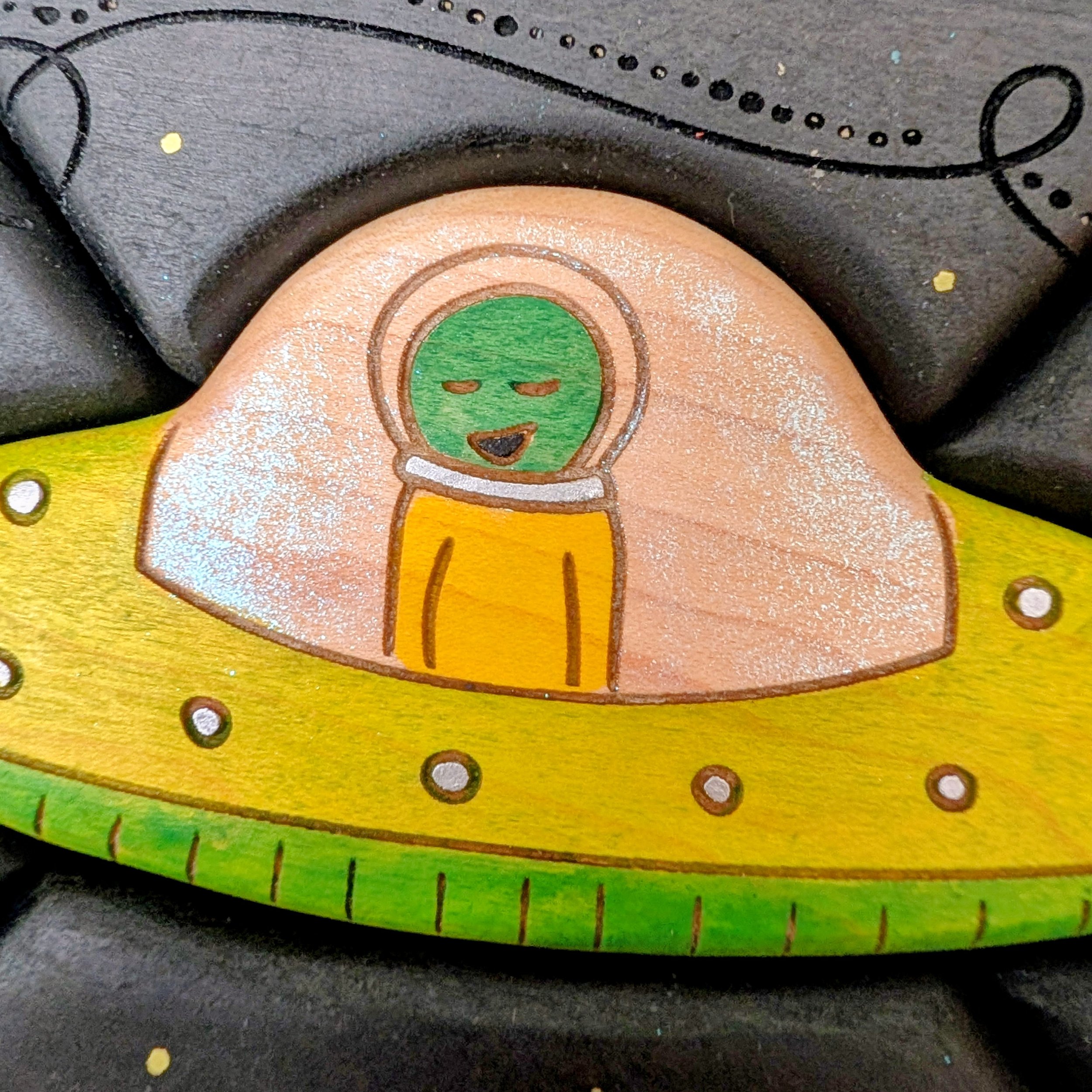 Green alien in yellow spacesuit inside wooden UFO puzzle piece
