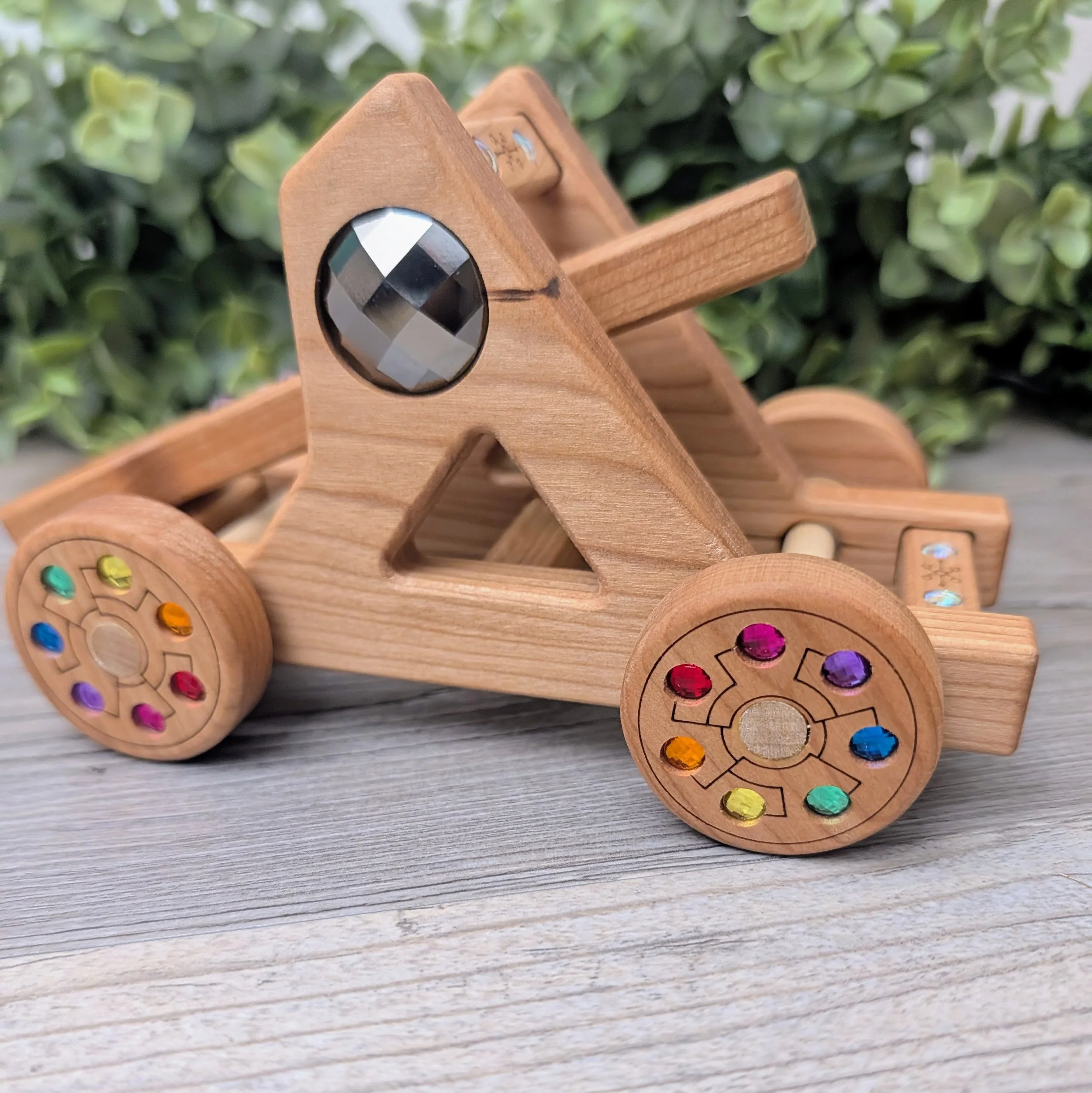 Cherry wood toy catapult featuring inset rainbow gem details