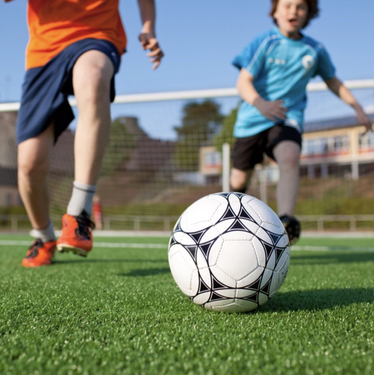 Children playing soccer on a green field with a goal in the background, focusing on a black and white soccer ball in the foreground.