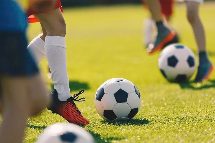 Close-up of soccer players' legs and feet on a grassy field with soccer balls, preparing for a game.