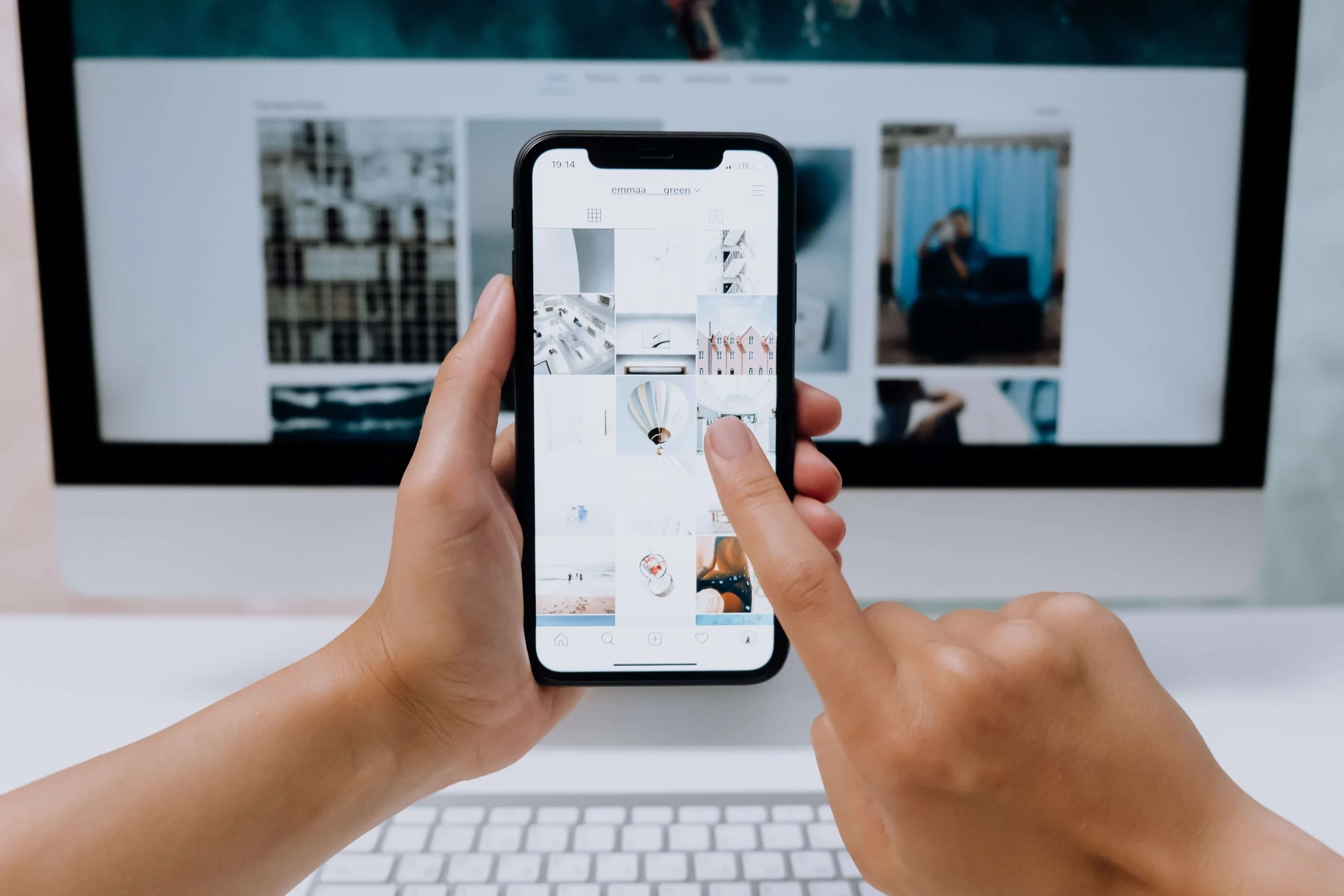 Image of Instagram on a persons phone and they are scrolling through it. It is also in the background on a computer.