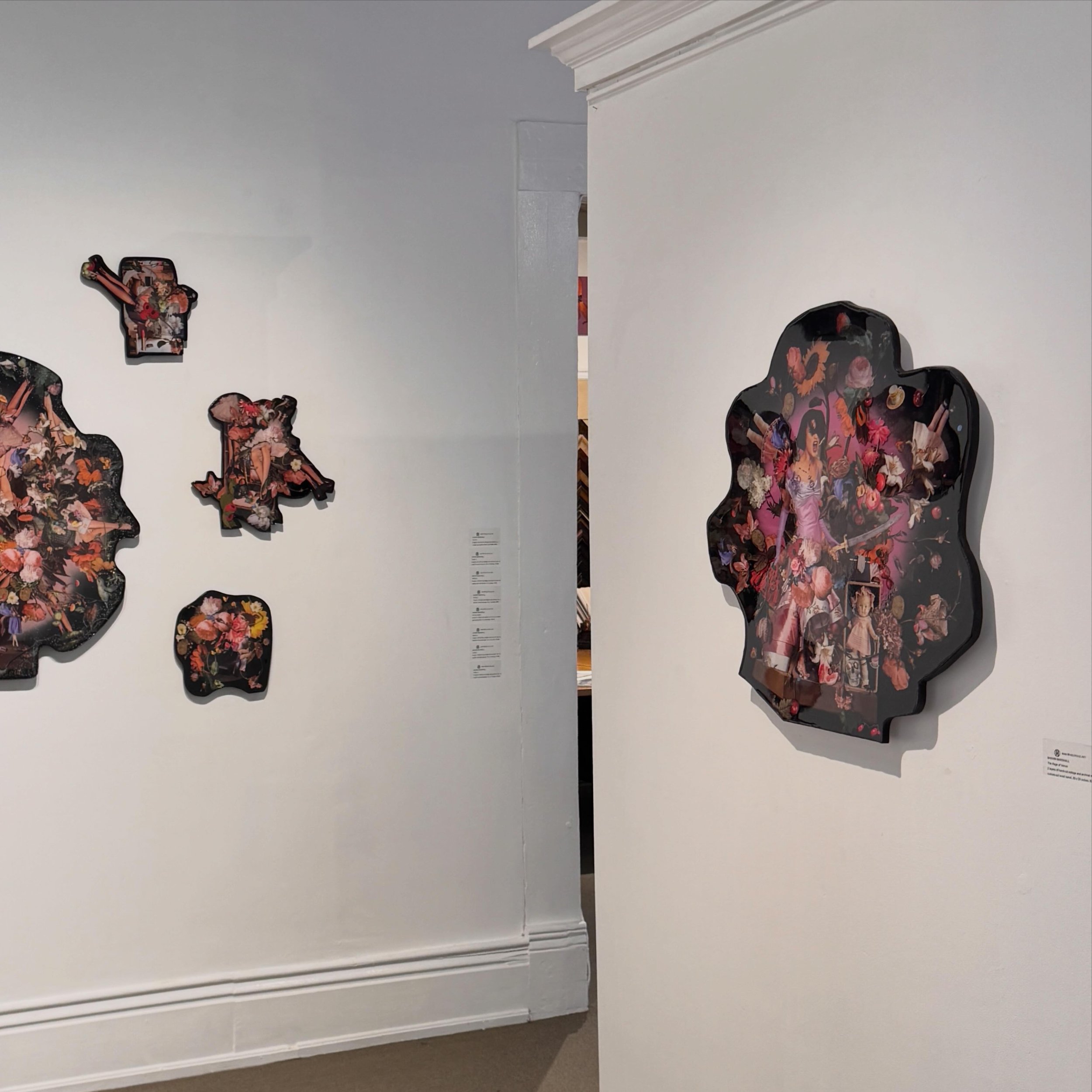 Interior view of a room with white walls, white crown molding, and baseboard trim. Several floral and fashion-themed paper cutouts are attached to the wall. Part of a white table or counter is visible at the right edge of the image.