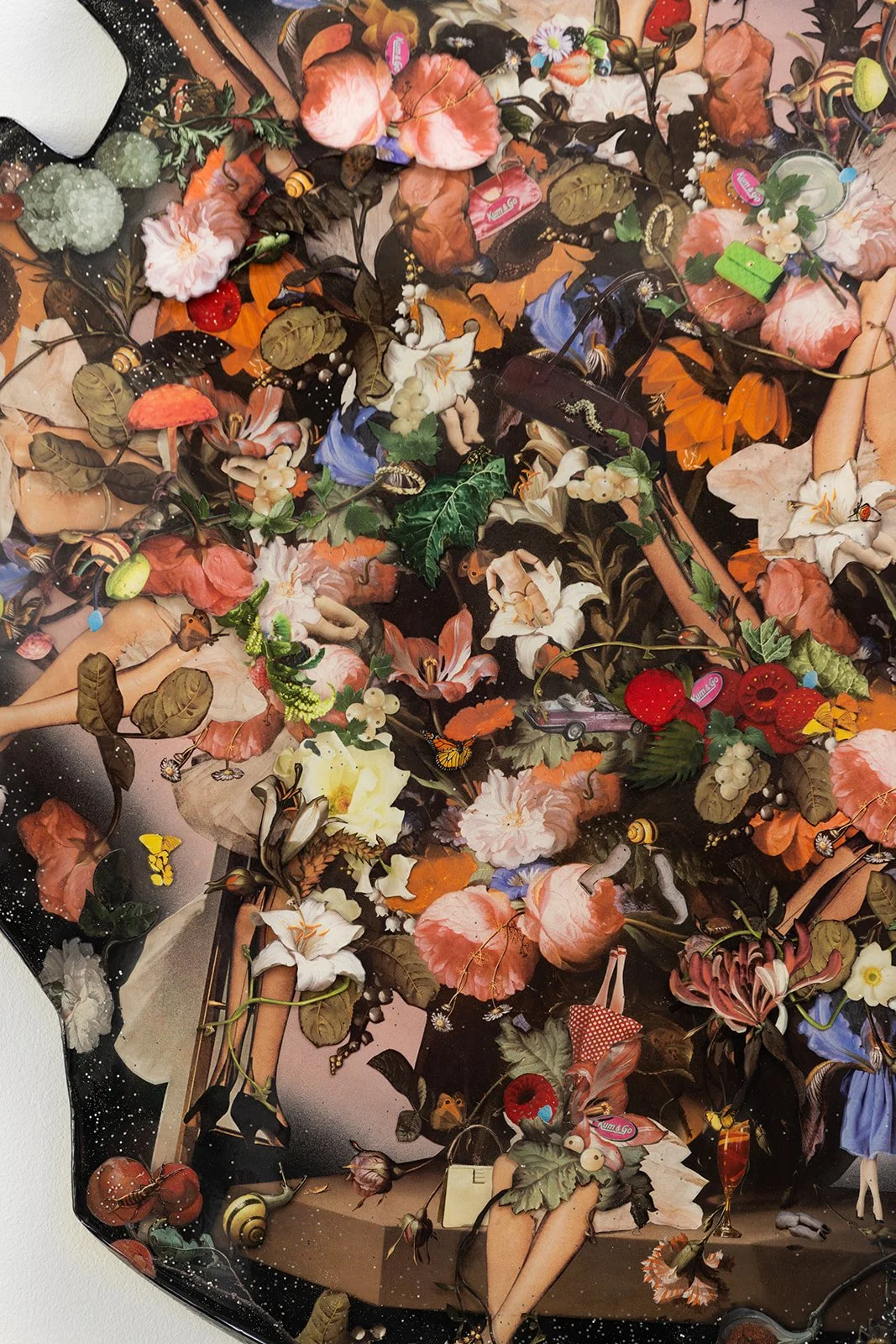 Mixed collage of artificial flowers, small toys, tiny dolls, butterflies, and miniature objects on a dark background.