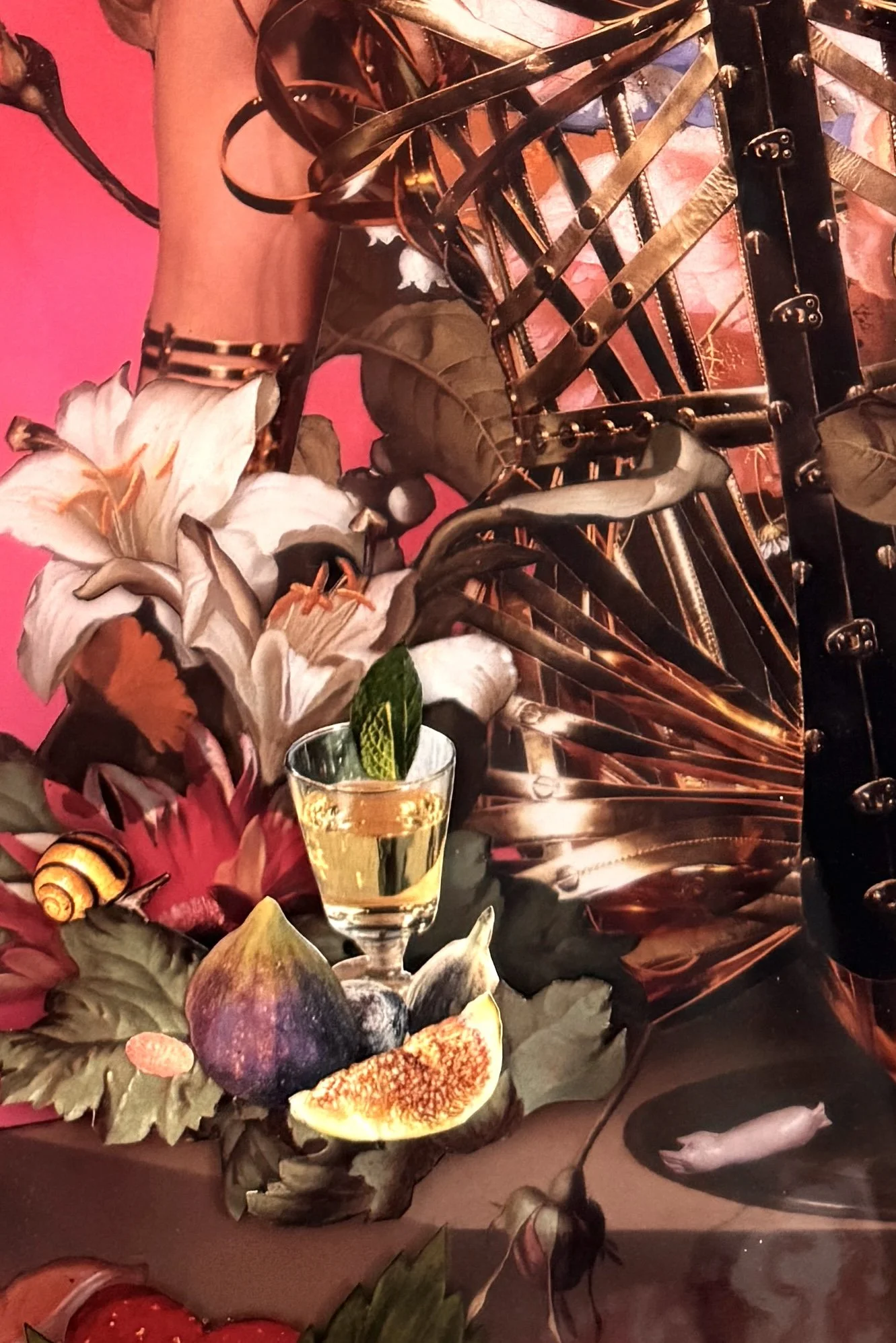 A floral arrangement with lilies, figs, and other flowers surrounding a glass of yellow liquid with a mint leaf. The background features a red-pink wall with metallic decorative elements.