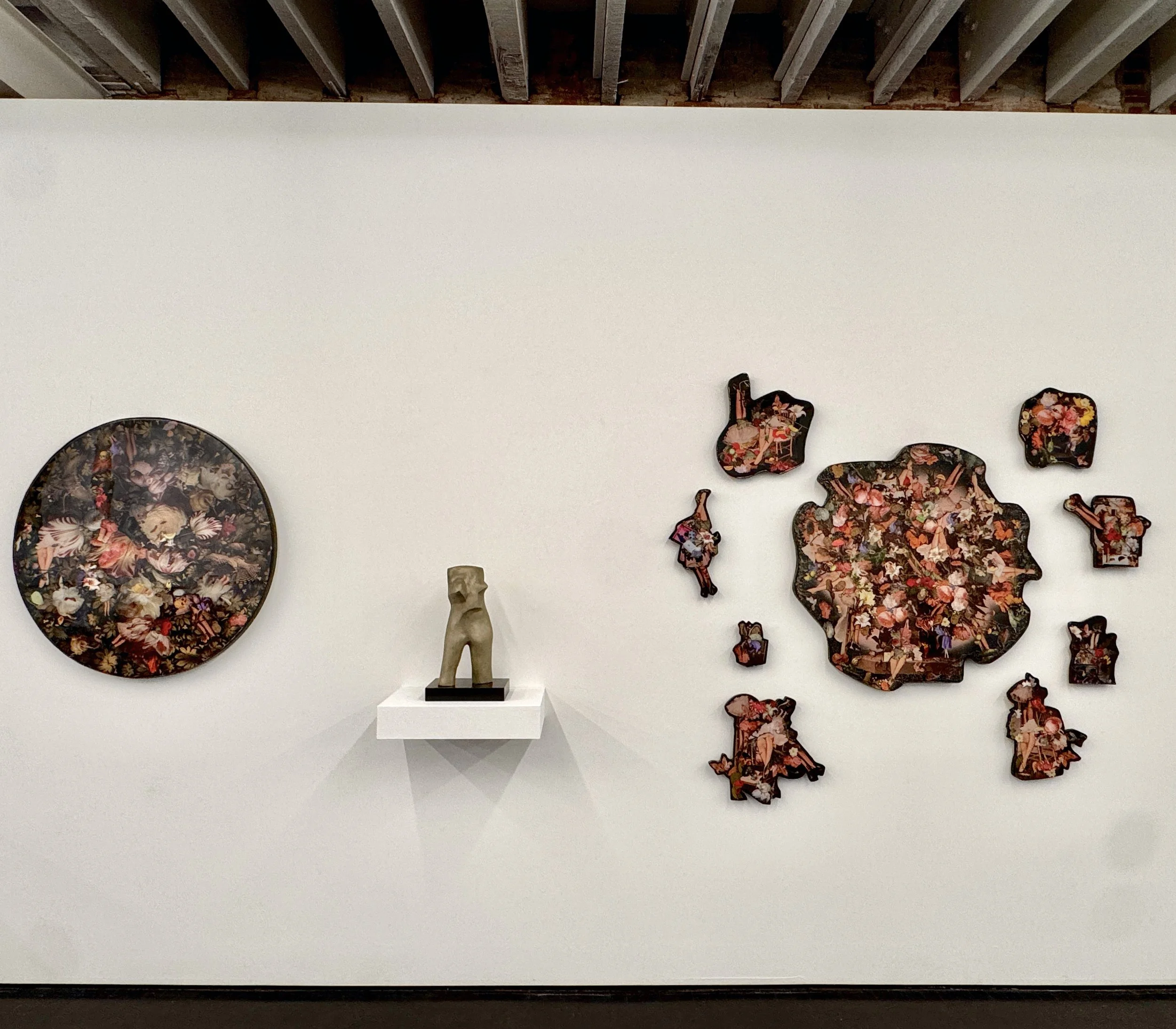 Gallery wall with brightly colored floral artwork, a white mannequin bust on a white pedestal, and a partial view of a floral-patterned vase.