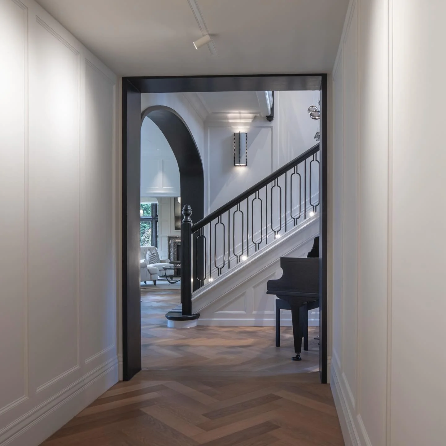 Monochrome meets understated luxury✨🖤
A palette of gentle contrasts; 
Crisp panelled walls, frame a herringbone floor that anchors the corridor with quiet warmth, while the sculptural staircase draws the eye forward and into the heart of the home ✨?