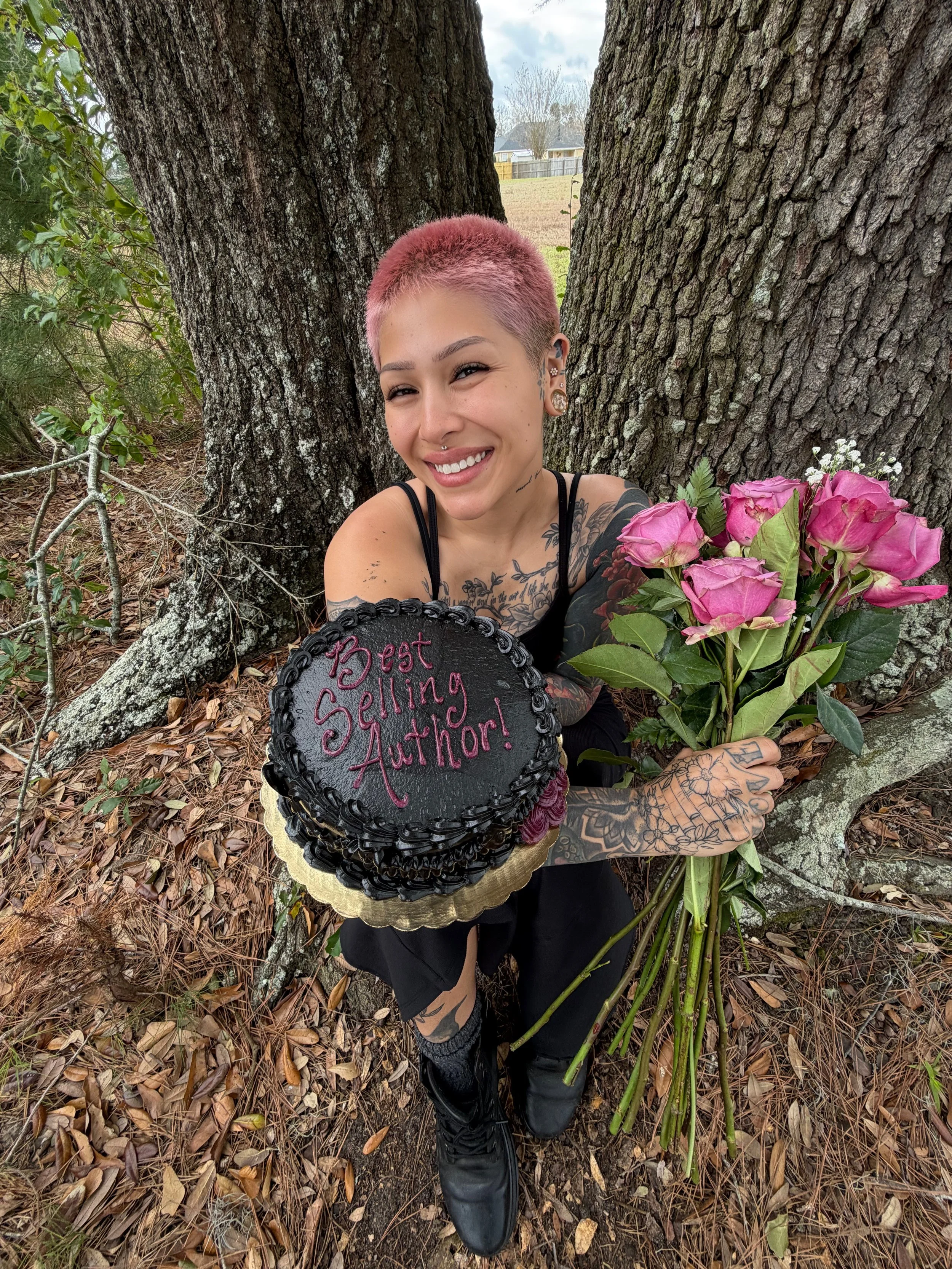 Young woman with short dark hair, glasses, and earrings in an art studio with paintings and art supplies in the background.