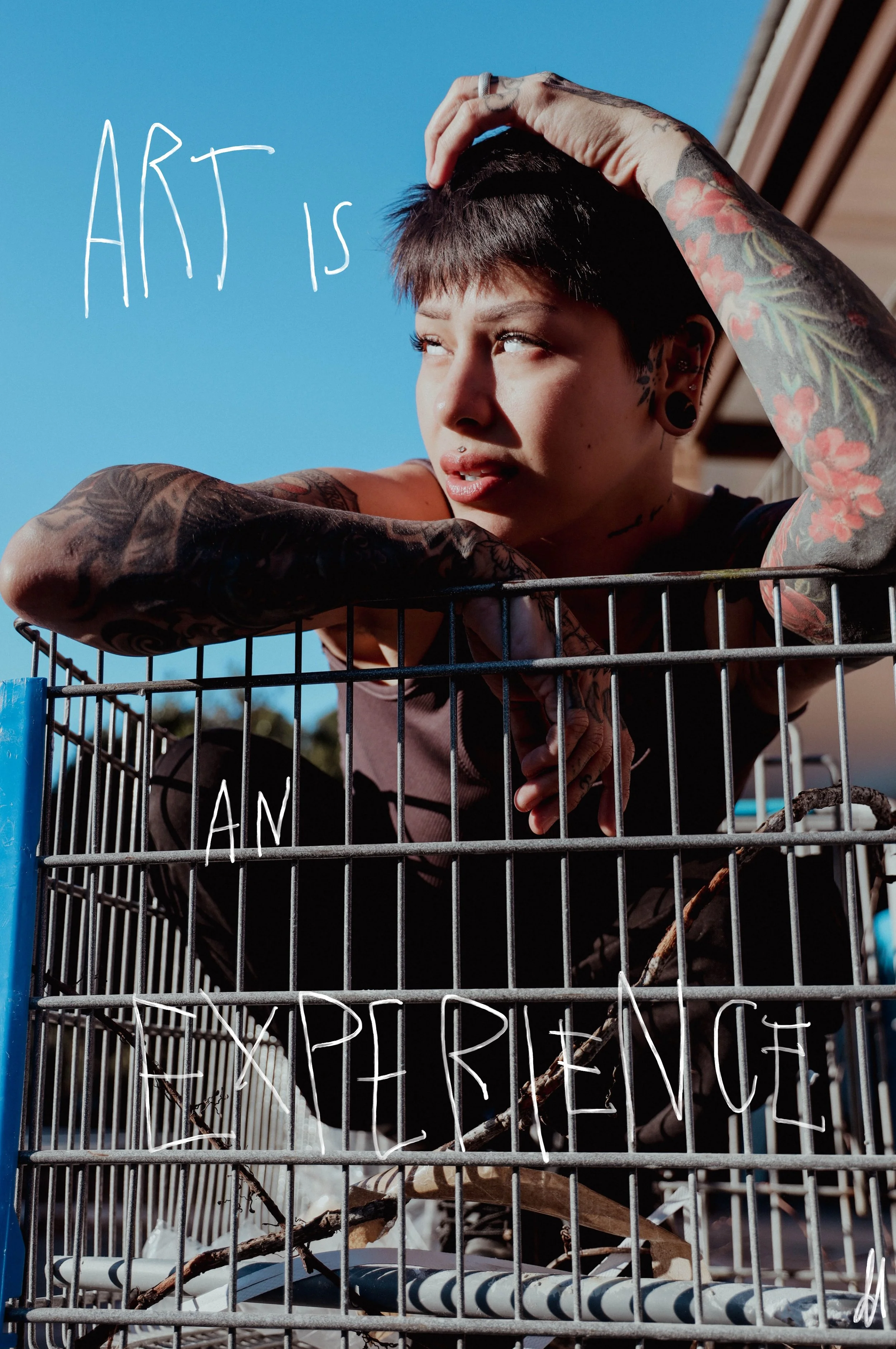 A tattooed woman with short dark hair leaning on a shopping cart, looking into the distance, with the words "ART IS AN EXPERIENCE" written in white on the cart.