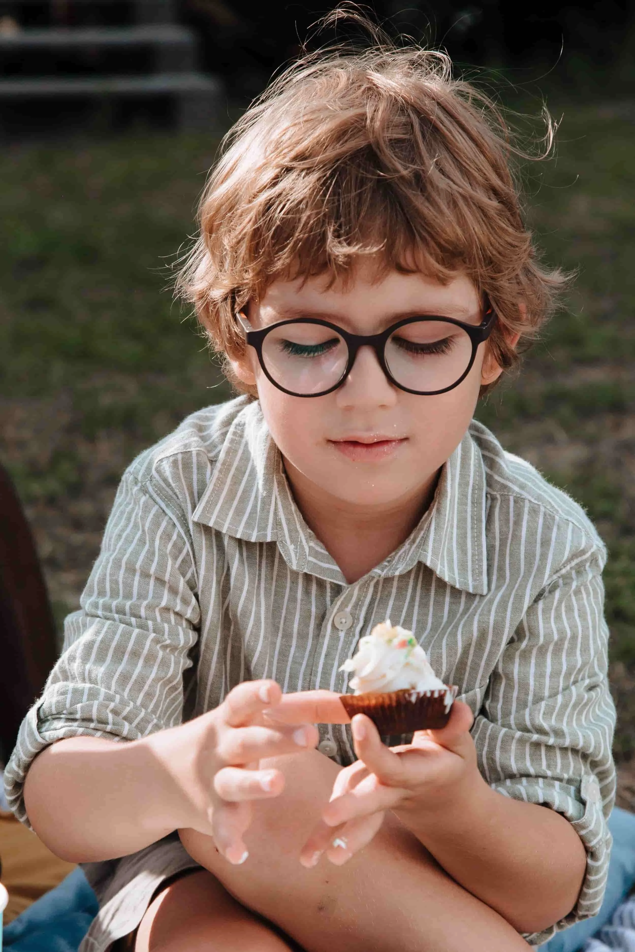 Young boy with glasses eating a cupcake