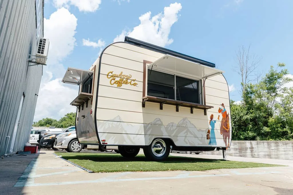 A vintage-style food truck with a mountain range mural and the sign "California Coffee" on a parking lot.