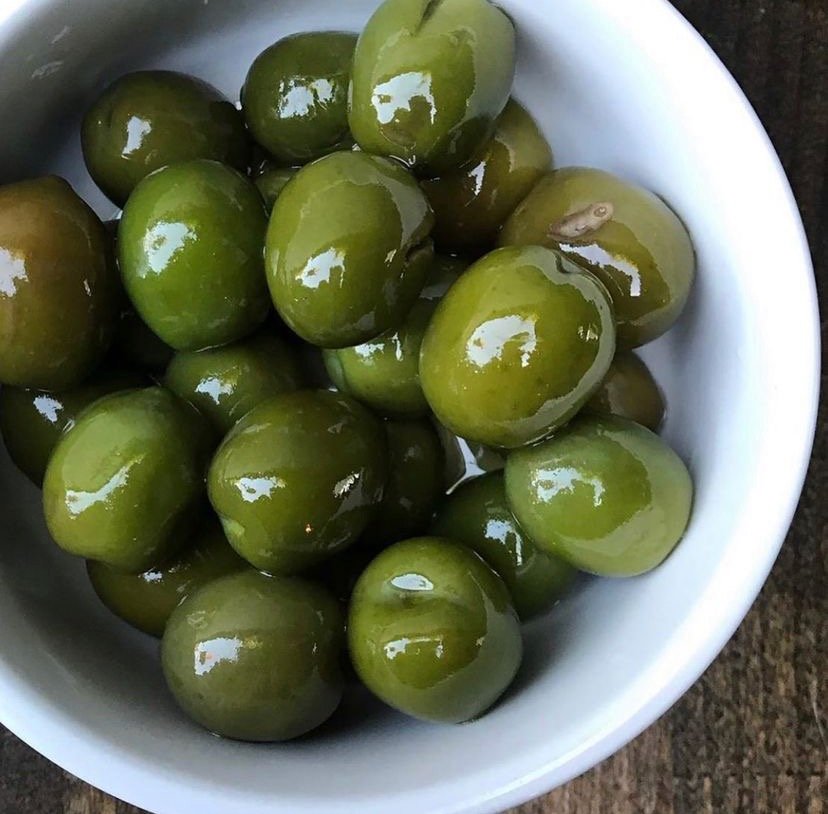A white bowl full of glossy green olives.