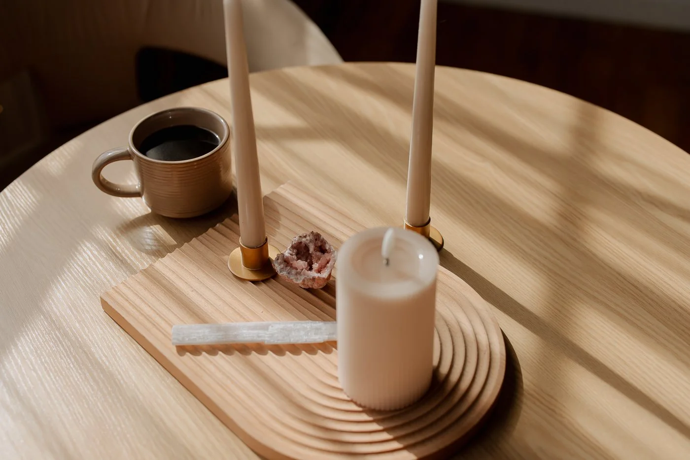 Decorative wooden table centerpiece with candles, a mug of coffee, quartz crystal, and a white ruler.