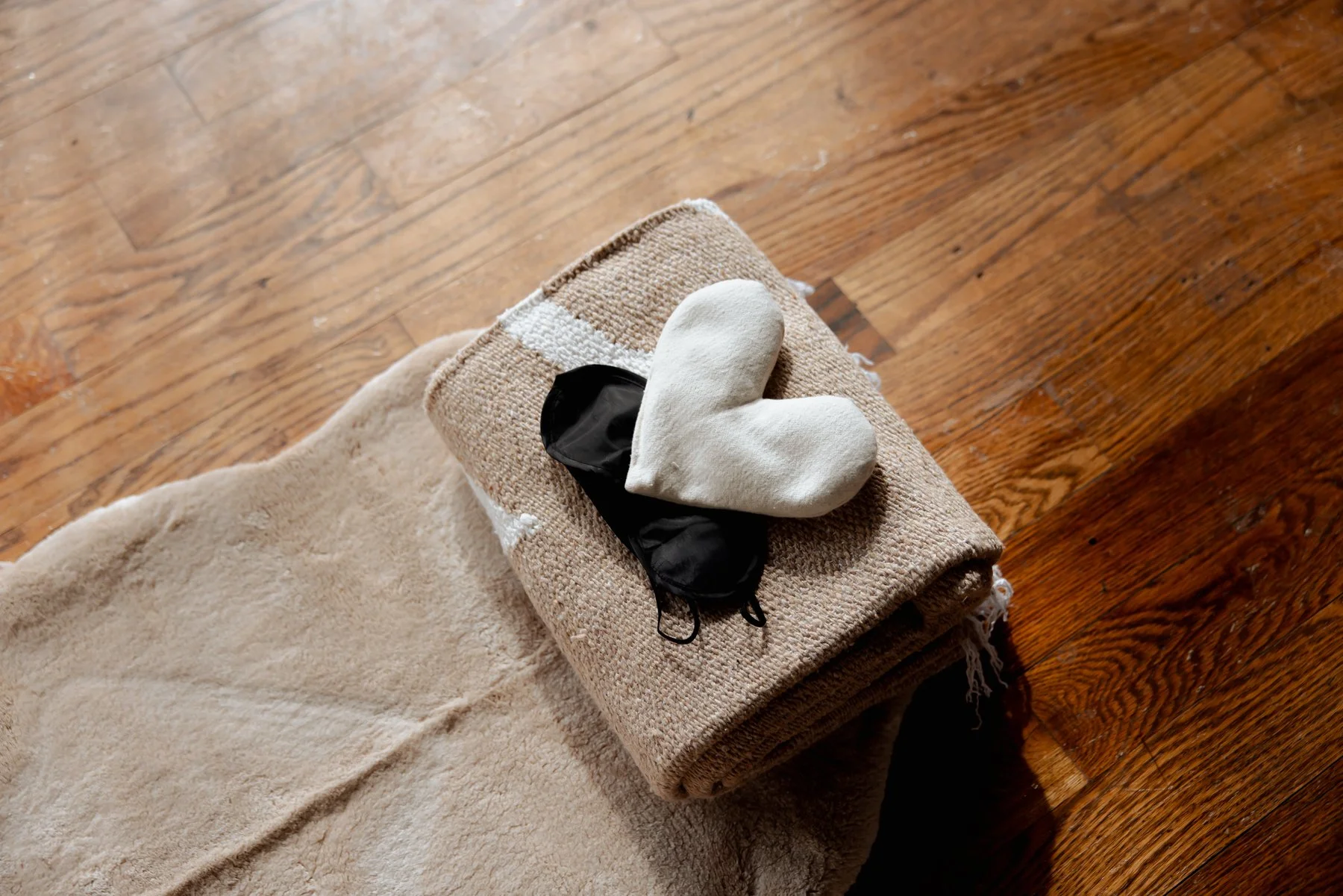 A beige rolled-up blanket or towel on a wooden surface with a white oven mitt and a black drawstring bag on top, near a beige carpet.