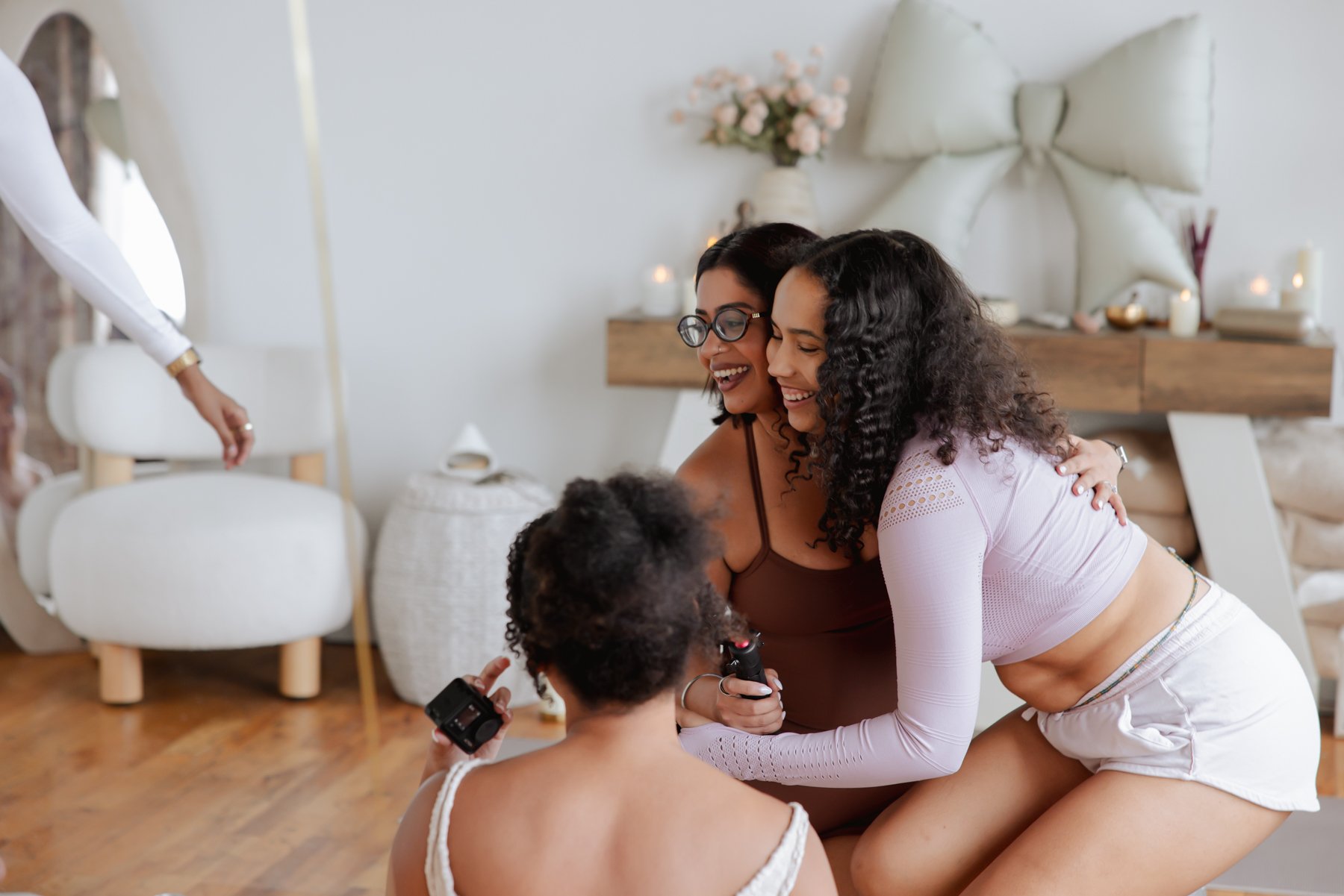Two women hugging and smiling with two children holding cameras in a cozy, decorated living room.