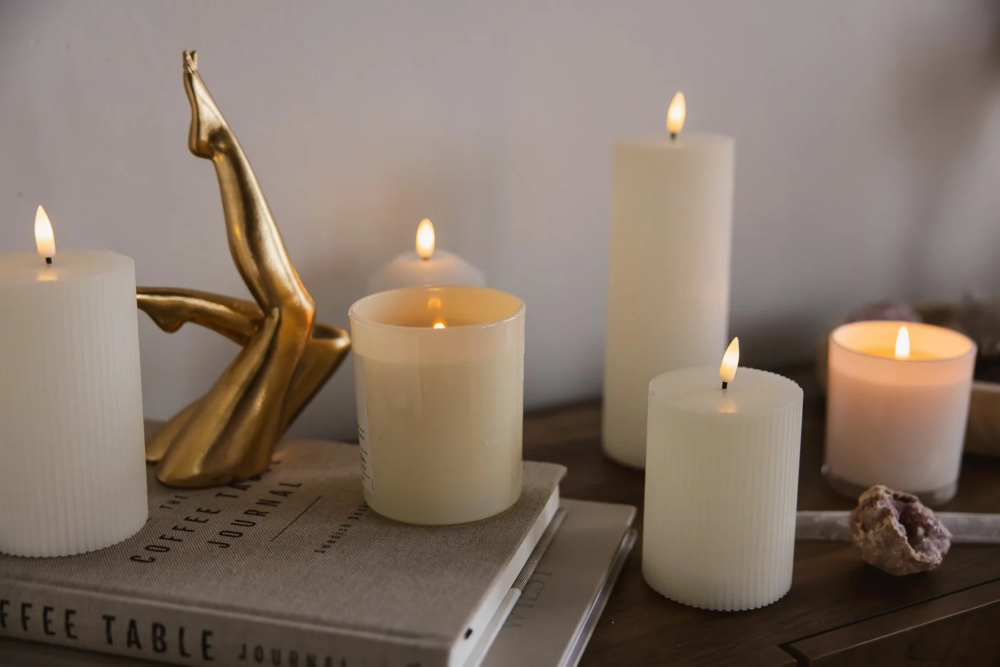 A collection of lit candles, a gold hand sculpture, a closed book, and a rose quartz crystal on a wooden table.