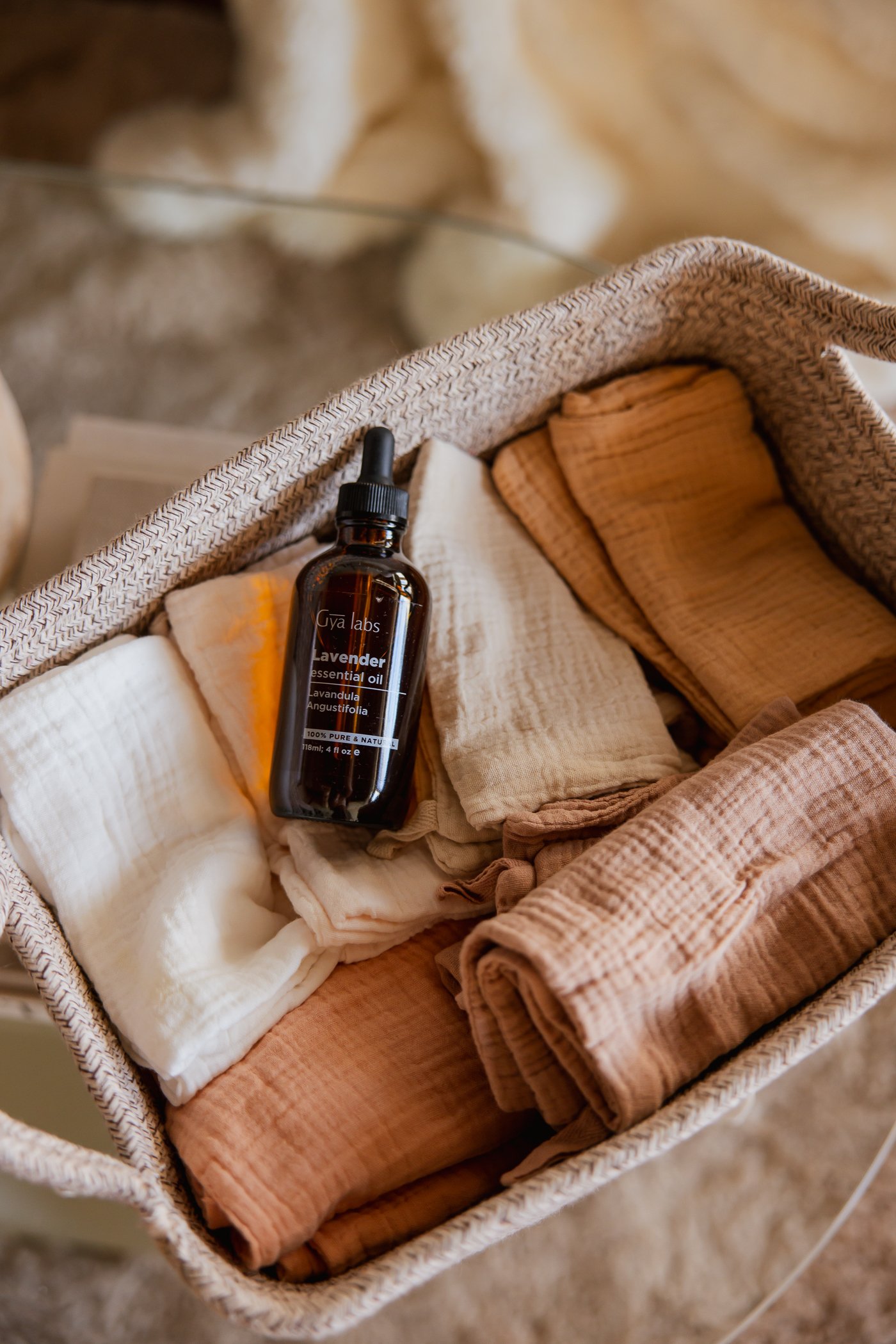 A basket containing folded towels in neutral tones and a brown bottle of lavender essential oil.