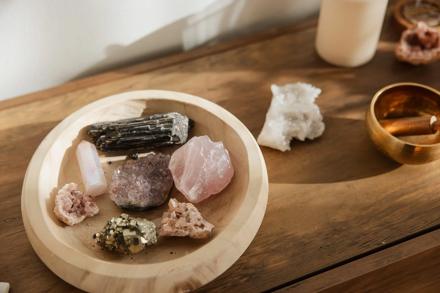 Various crystals and mineral specimens on a wooden surface, including quartz, pyrite, and other mineral fragments, with a candle on the table.