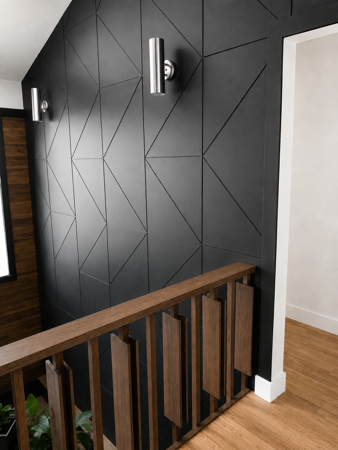 Interior view of a staircase with a wooden handrail and decorative wood panels on the balustrade, next to a dark geometric tiled wall with modern cylindrical wall sconces, and a light-colored floor with white baseboard.
