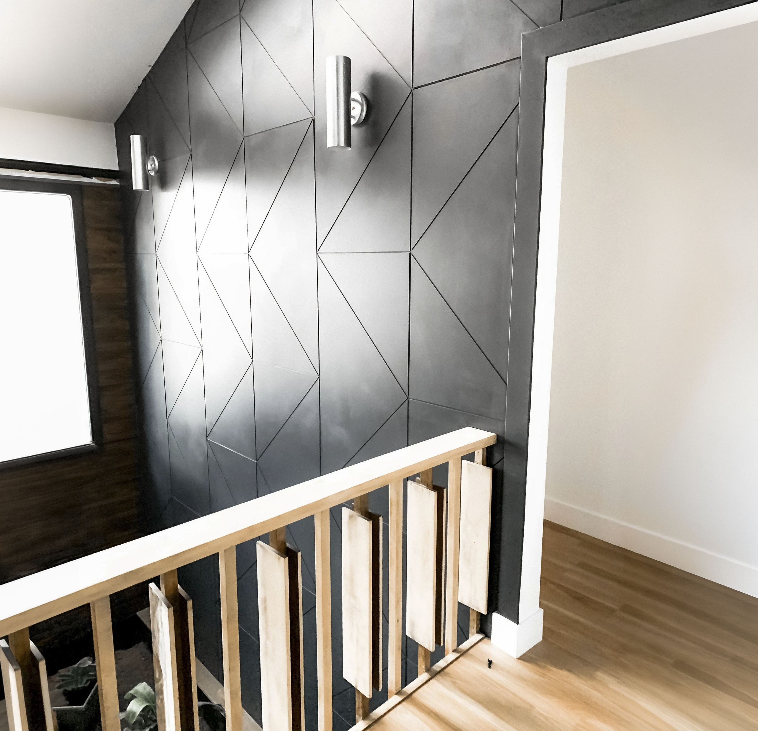Interior view of a modern space with black geometric tiled wall, wooden railing, wood flooring, and a white doorway.