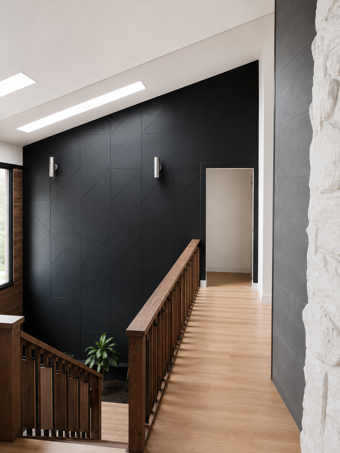 Interior view of a modern staircase landing with light wood flooring, a black feature wall with geometric paneling, two wall-mounted silver lights, a partial stone accent wall on the right, and a small green plant at the base of the staircase.