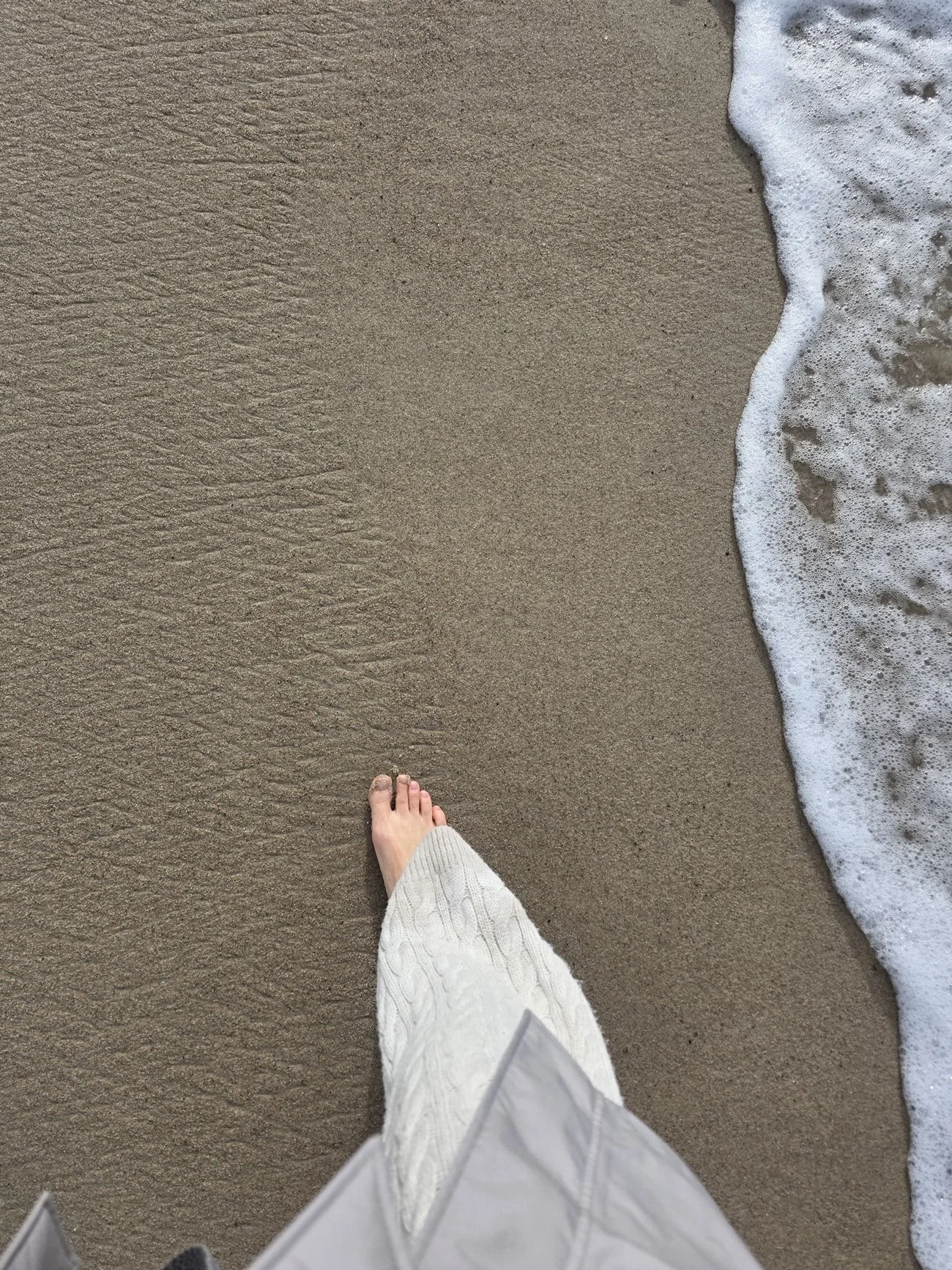 woman in a classic outfit bare feet walking on the sand with ocean wave on the side