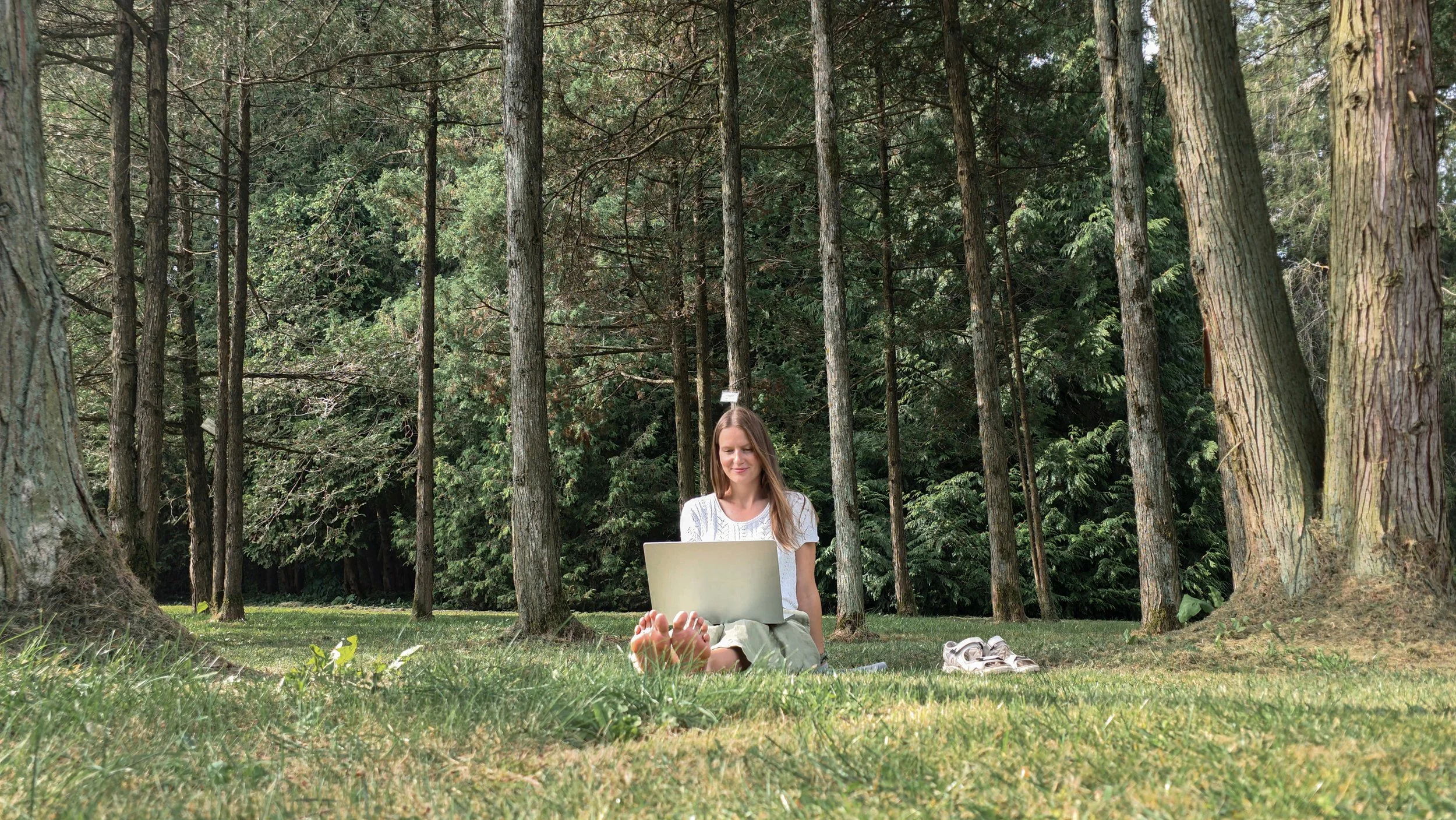 Bonethica founder smiling sits with her computer on her legs on the grass in the background of green trees