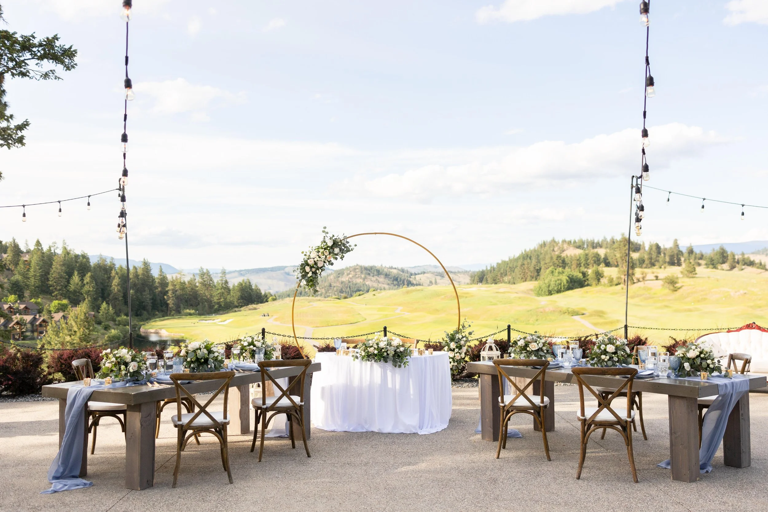 Outdoor wedding reception setup with decorated tables, chairs, string lights, and a scenic mountain view and golf course. Vernon BC. Predator Ridge Golf Course. Wedding planning by Day by Knight Events. Boketto Photography.