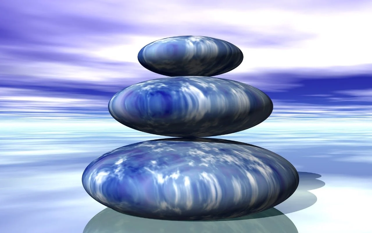 Stack of three smooth, blue stones on a reflective surface against a cloudy sky.
