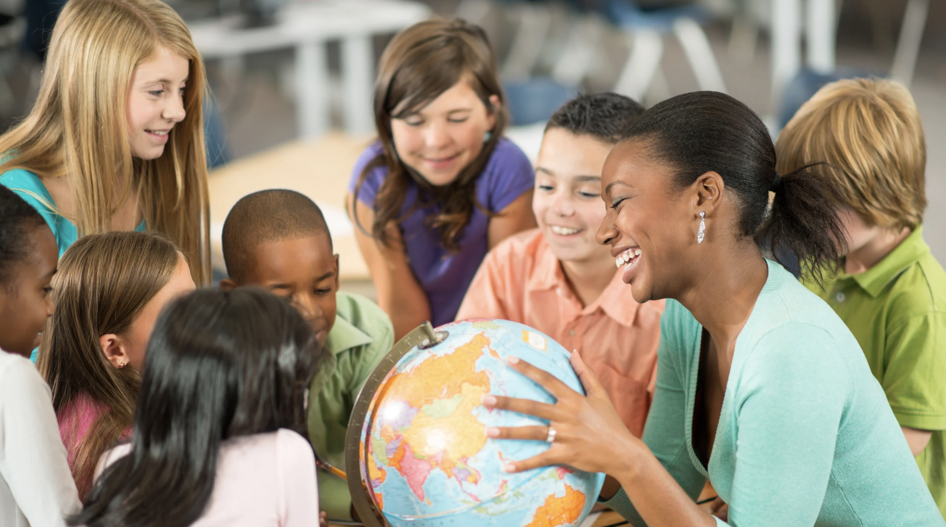 Teacher and diverse group of children looking at a globe in a classroom setting.