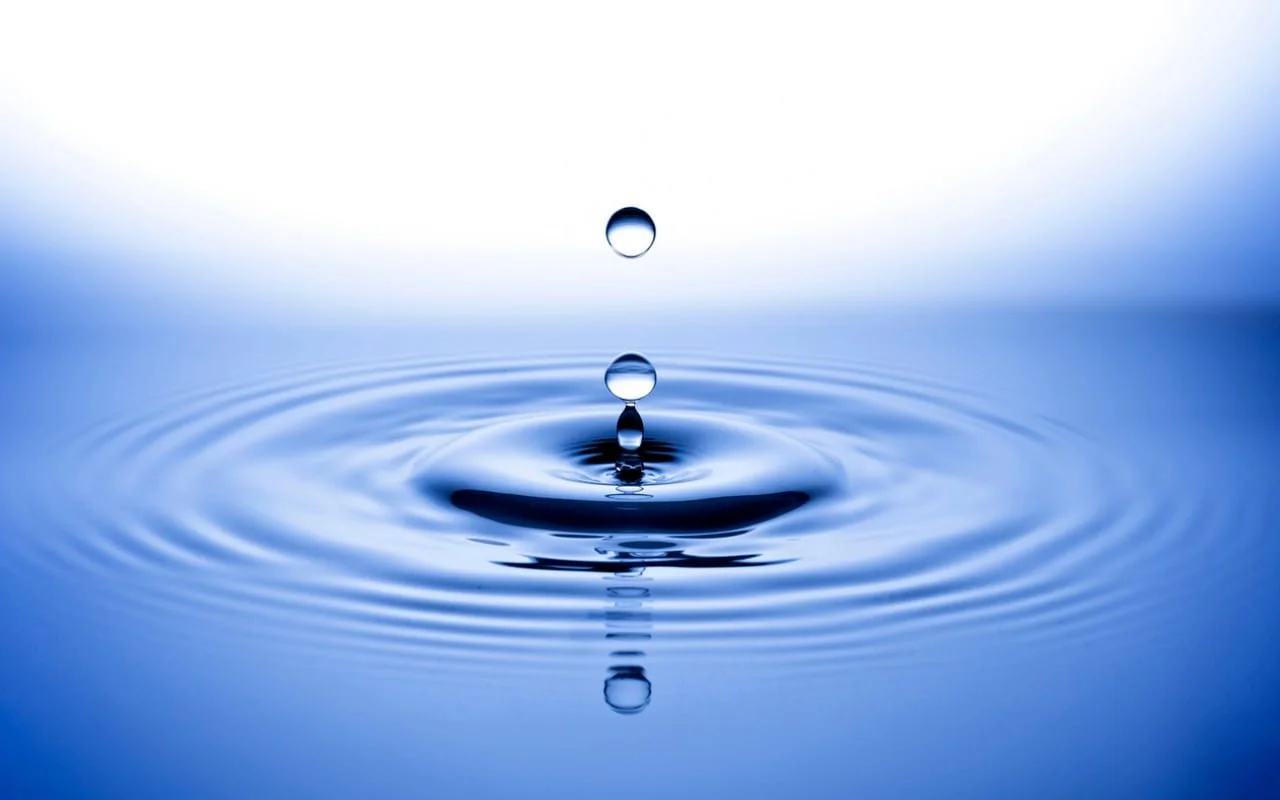 Water droplet creating ripples on a smooth blue water surface.