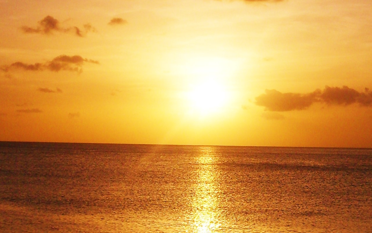 Golden sunset over the ocean with scattered clouds.