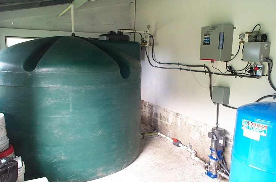 Large green water tank with connected piping and control panels in a utility room.