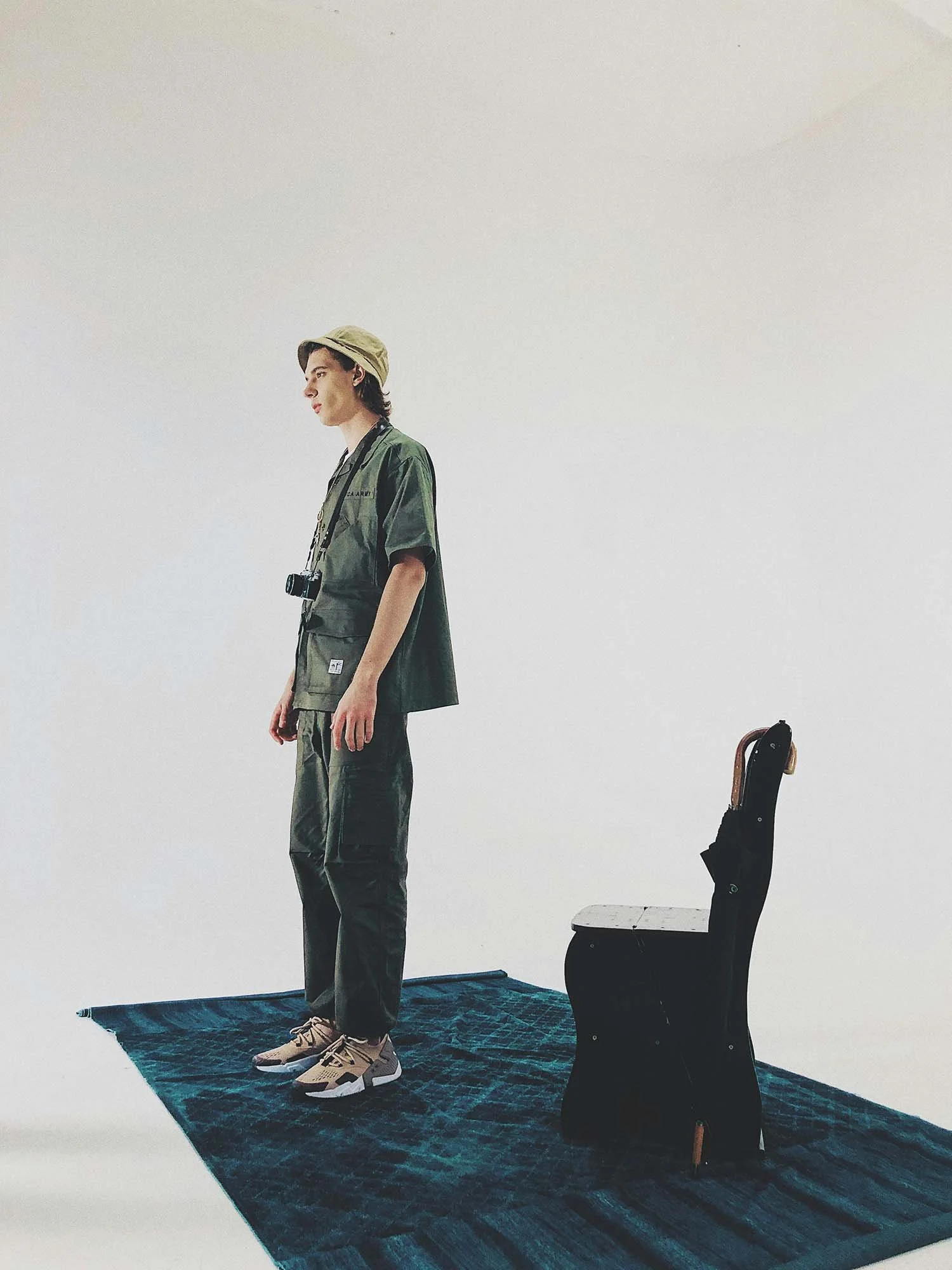 Young photographer standing in a photography studio with a blue rug and a chair.